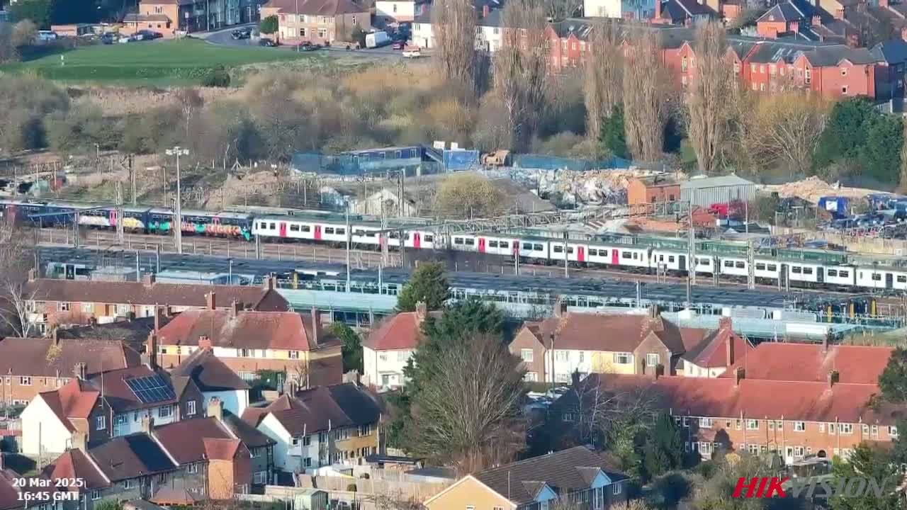 A long passenger train sits on tracks near a residential area on a sunny day.