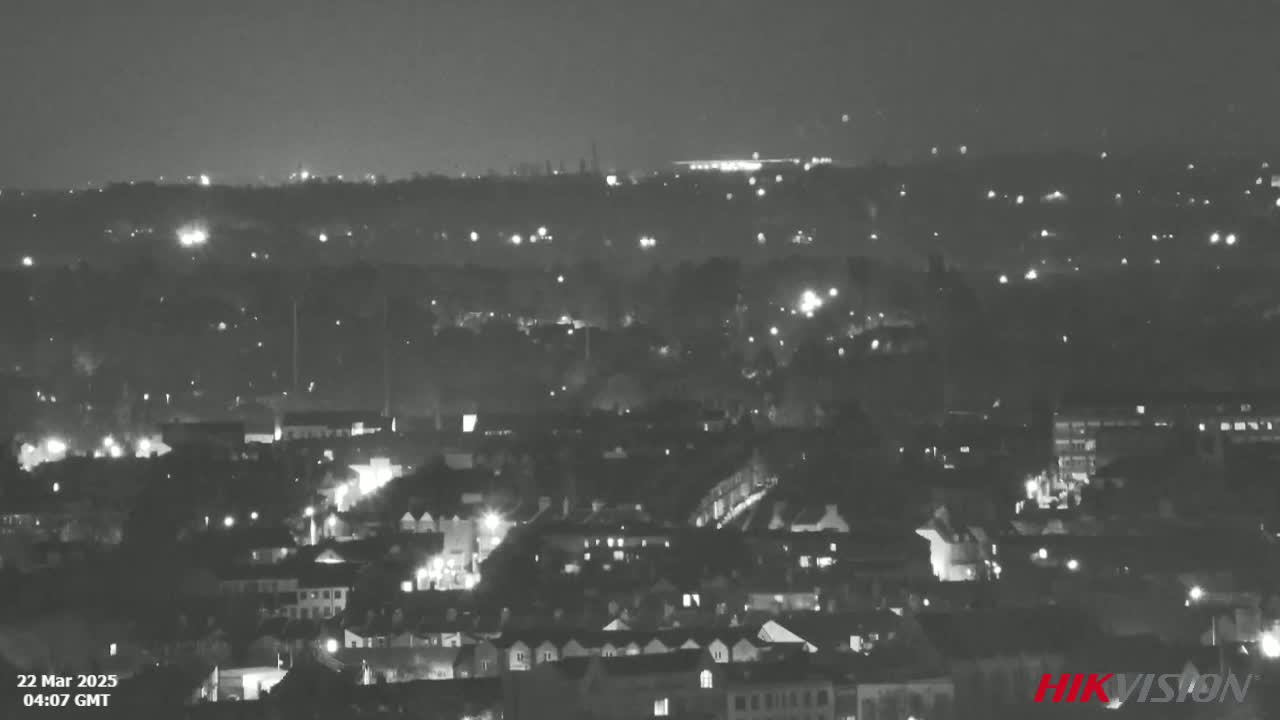 A nighttime, high-angle, black and white view of a city with scattered lights.