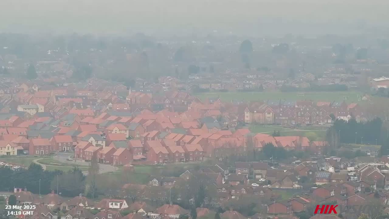 A hazy view shows a large residential area with many houses, mostly two stories and red-roofed, extending into the distance.