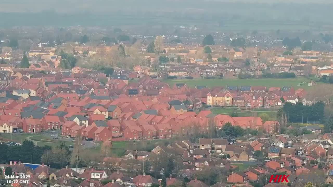 A sprawling suburban area with numerous red-roofed houses under a hazy sky.