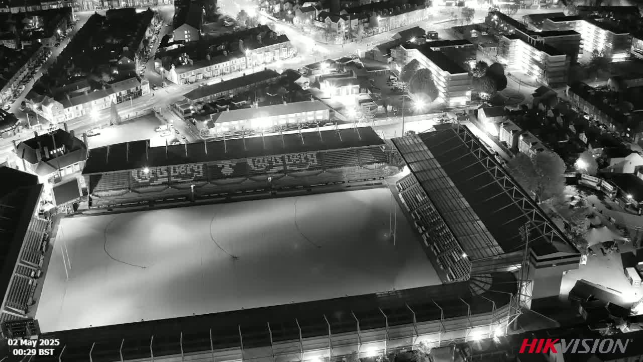 An aerial nighttime view of an empty sports stadium, surrounded by a residential area illuminated by streetlights.