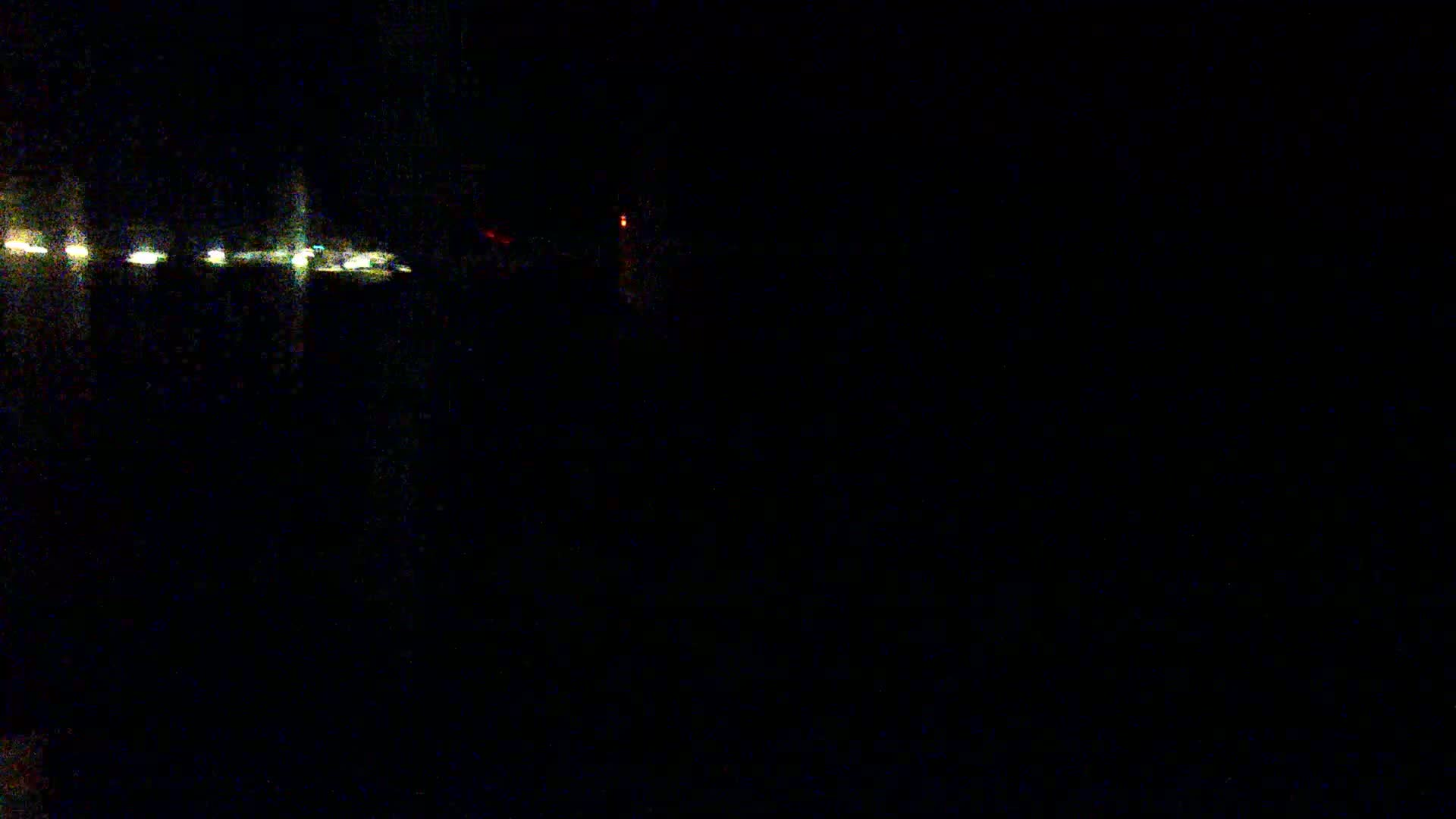 A dark, nighttime scene shows a line of distant lights, possibly from vehicles or buildings, with a single faint red light visible further away.