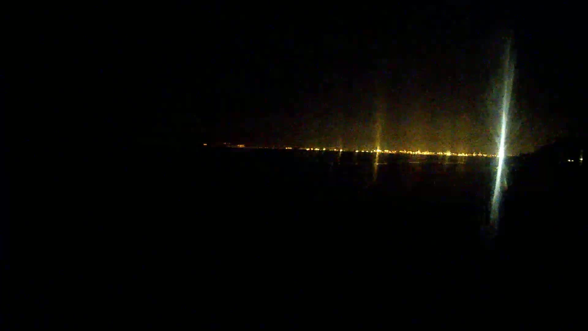 A distant city skyline illuminated at night is visible from a dark, presumably coastal, location.