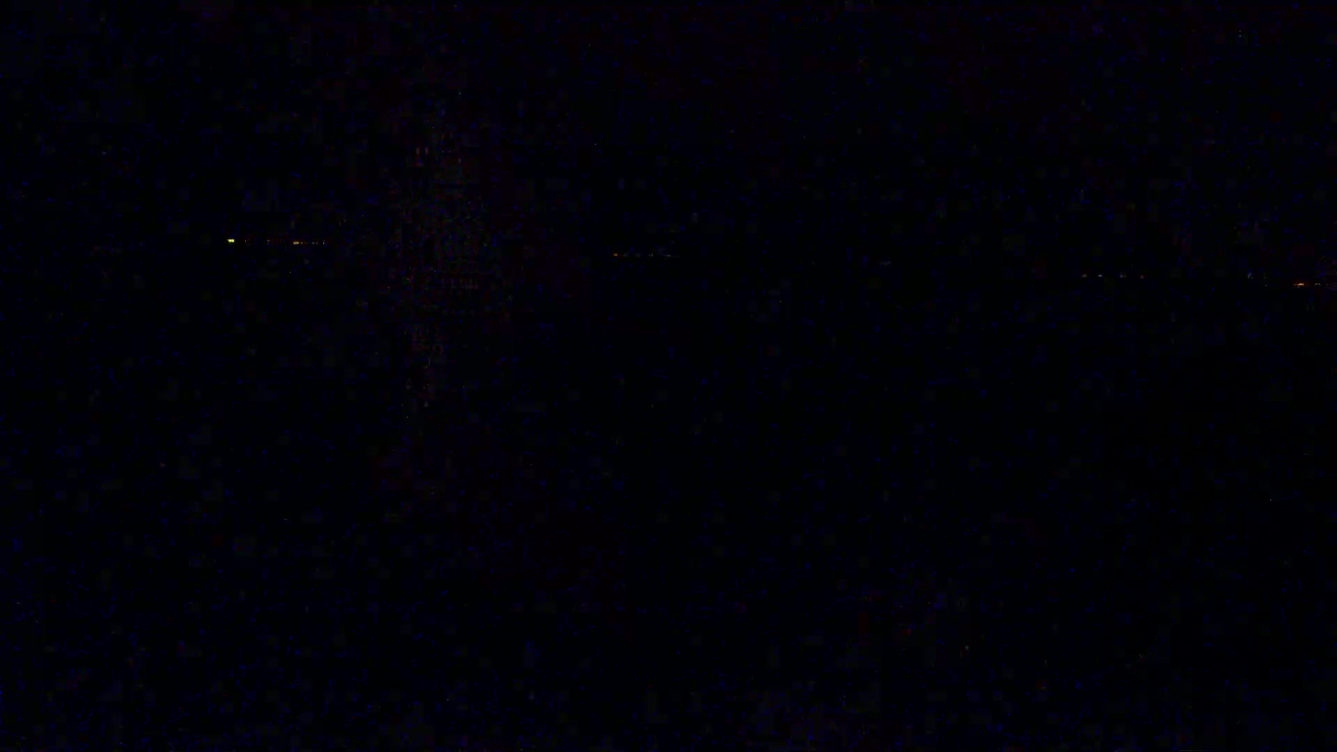 A dark, nighttime scene shows a distant line of faint, orange lights on the horizon.