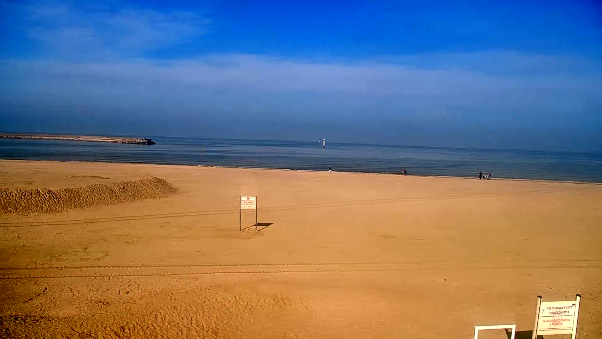 A wide sandy beach stretches to a calm sea under a clear blue sky.