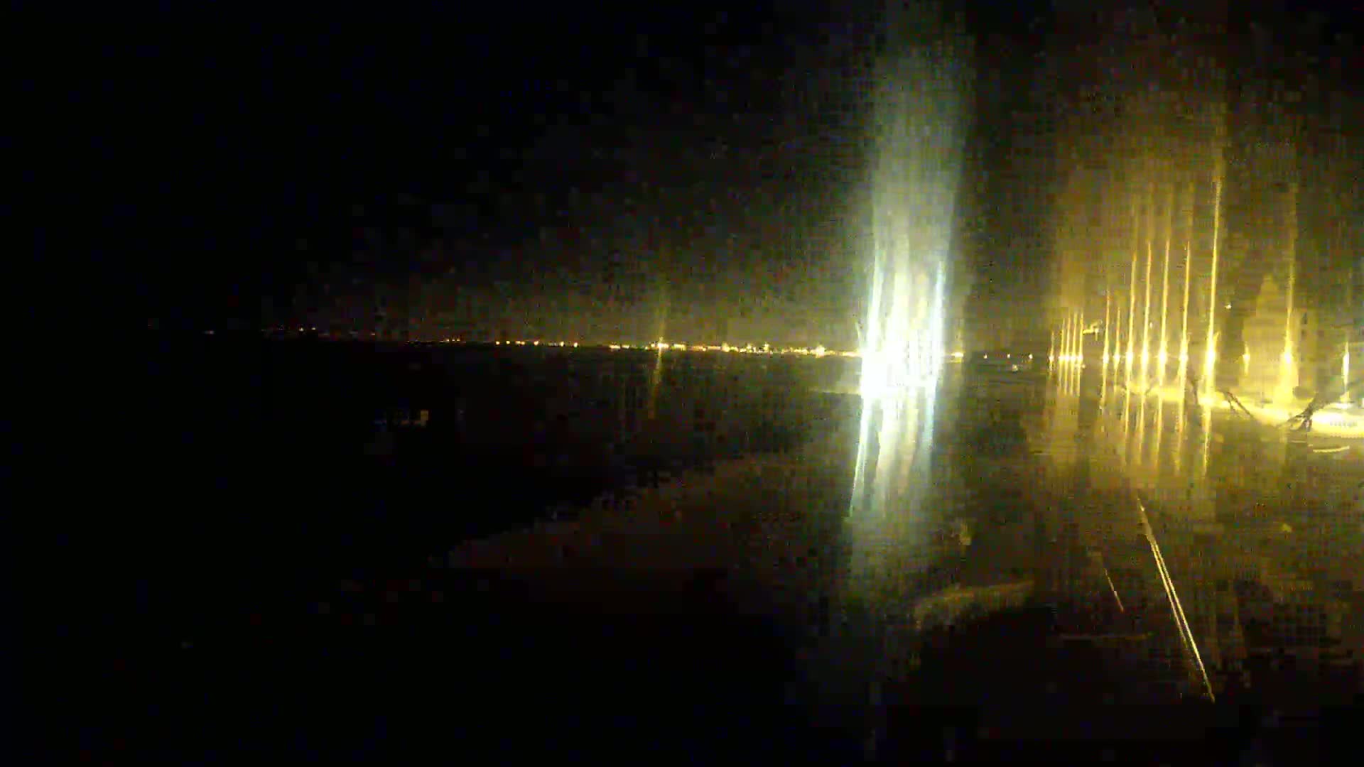 At night, a body of water reflects illuminated fountains and a distant cityscape.