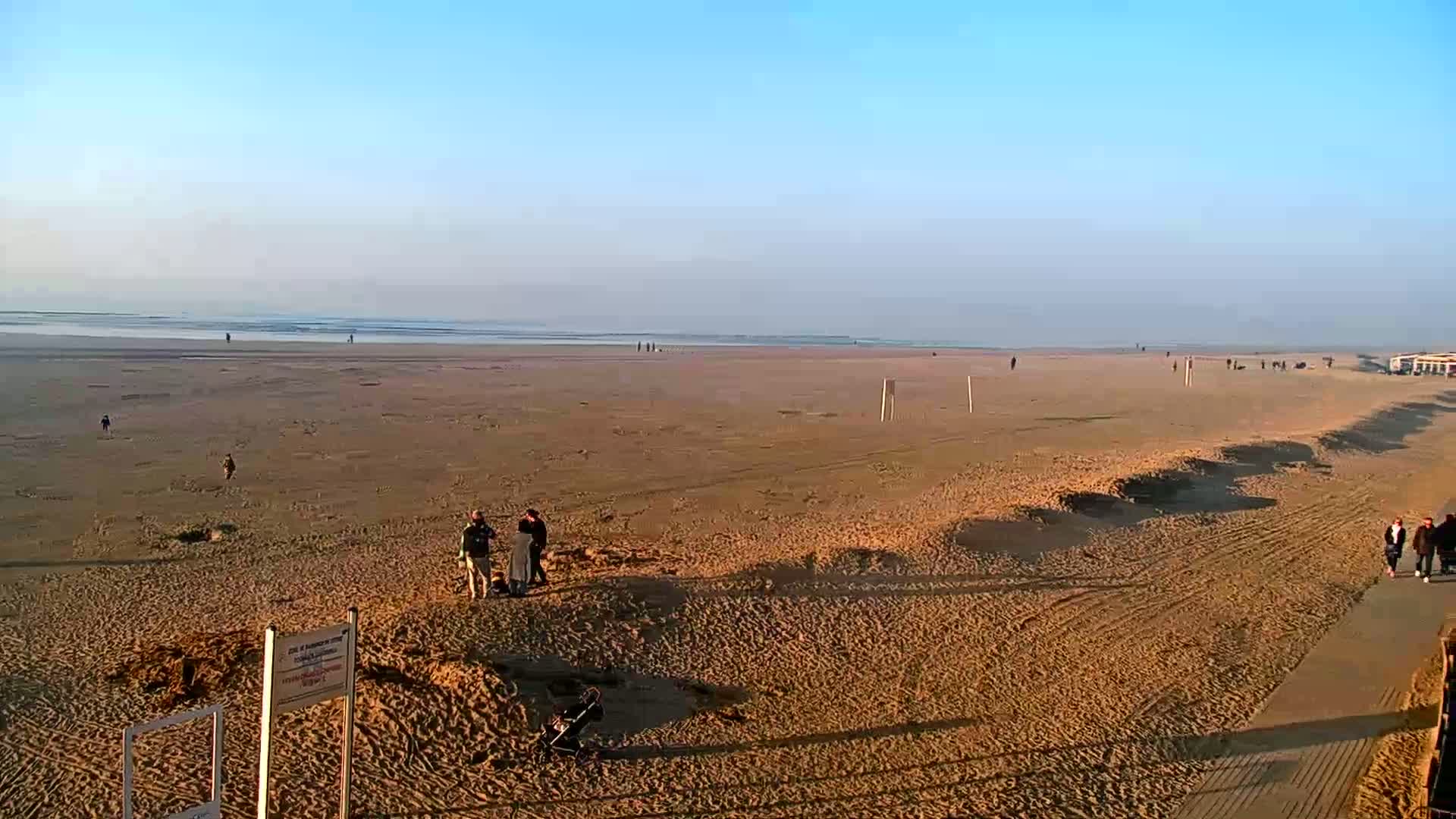 A wide sandy beach stretches to a calm ocean under a clear blue sky.