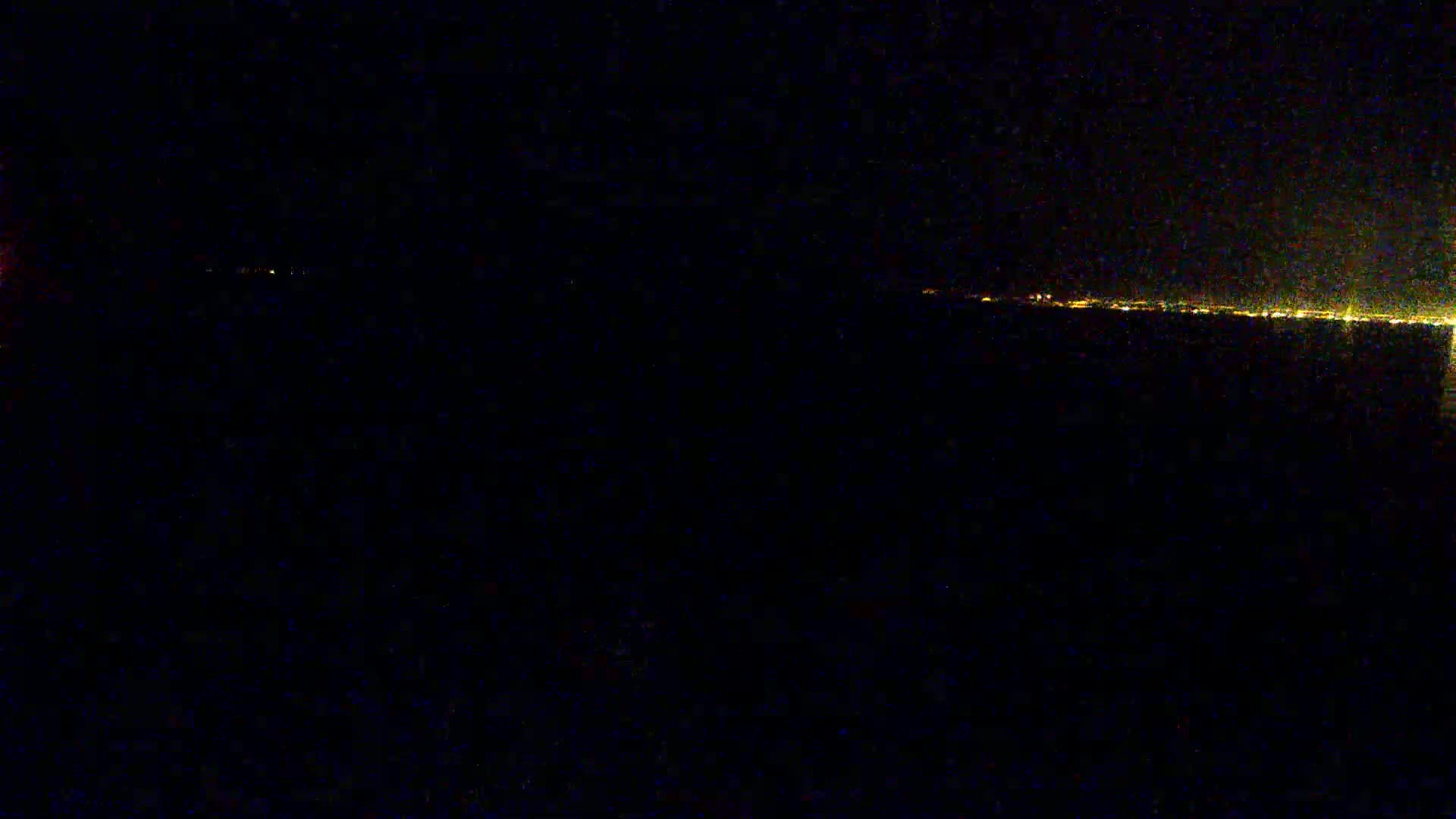 A distant city skyline is visible at night across a dark body of water under a clear sky.