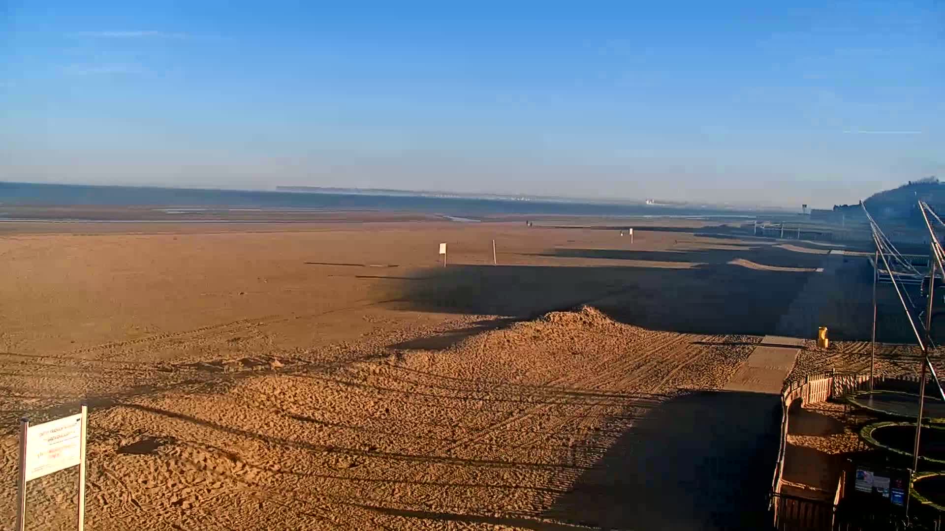 A wide sandy beach stretches to a calm sea under a clear blue sky.