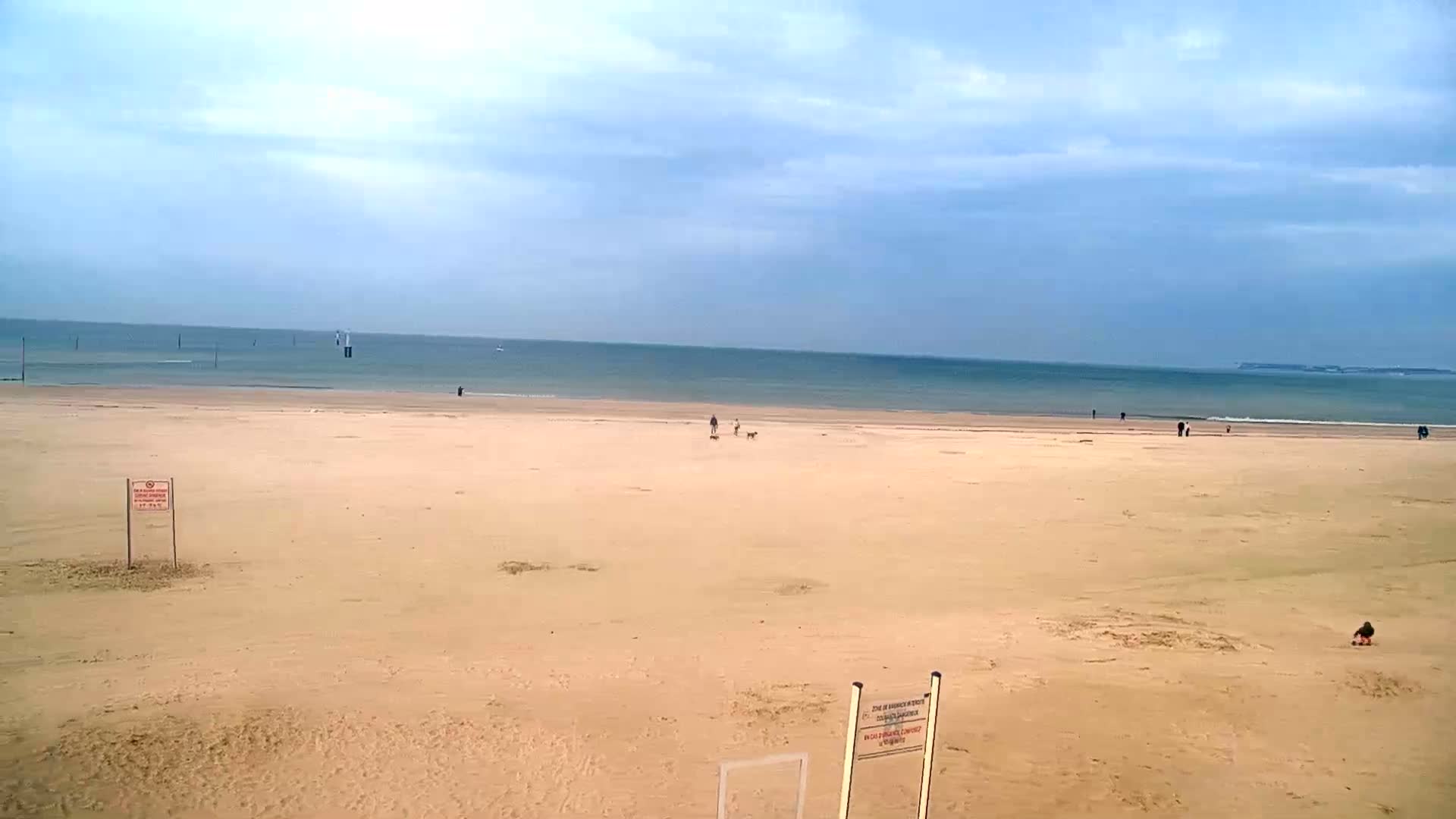 A wide sandy beach stretches to a calm, blue ocean under a mostly cloudy sky.