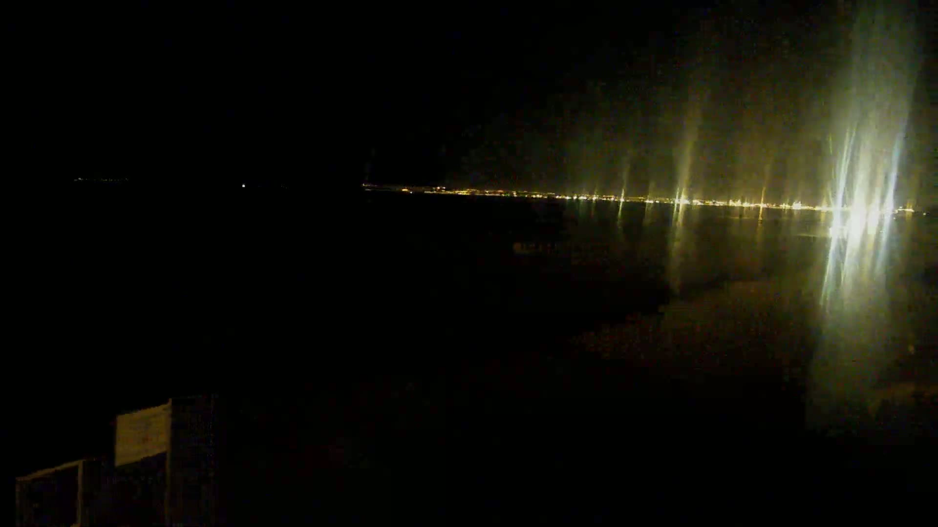 A nighttime view of a city's lights across a body of water, reflecting brightly on the dark surface.