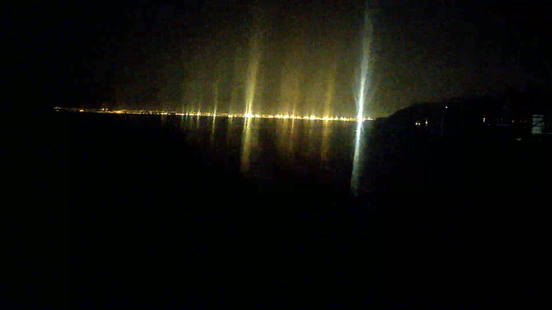 A nighttime view of a calm body of water reflecting the lights of a distant city.