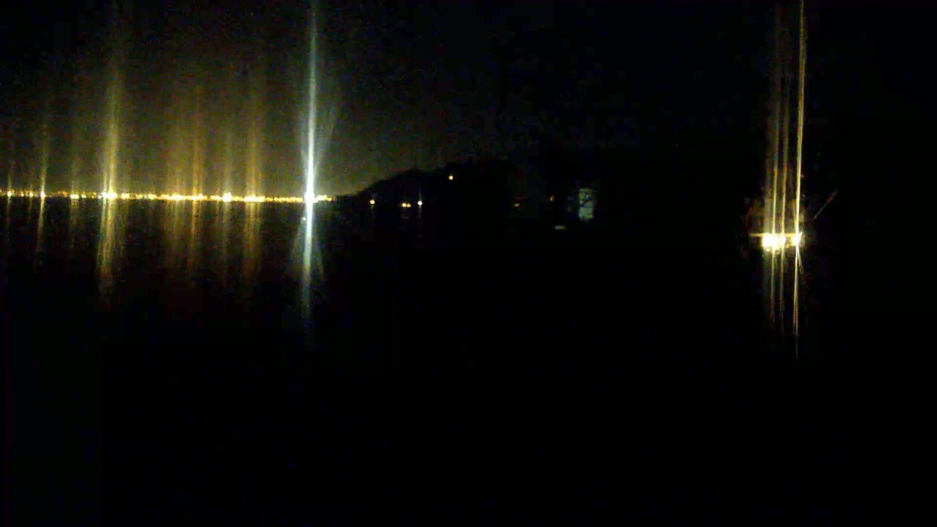 A nighttime view of a body of water reflecting the lights of a distant city skyline.
