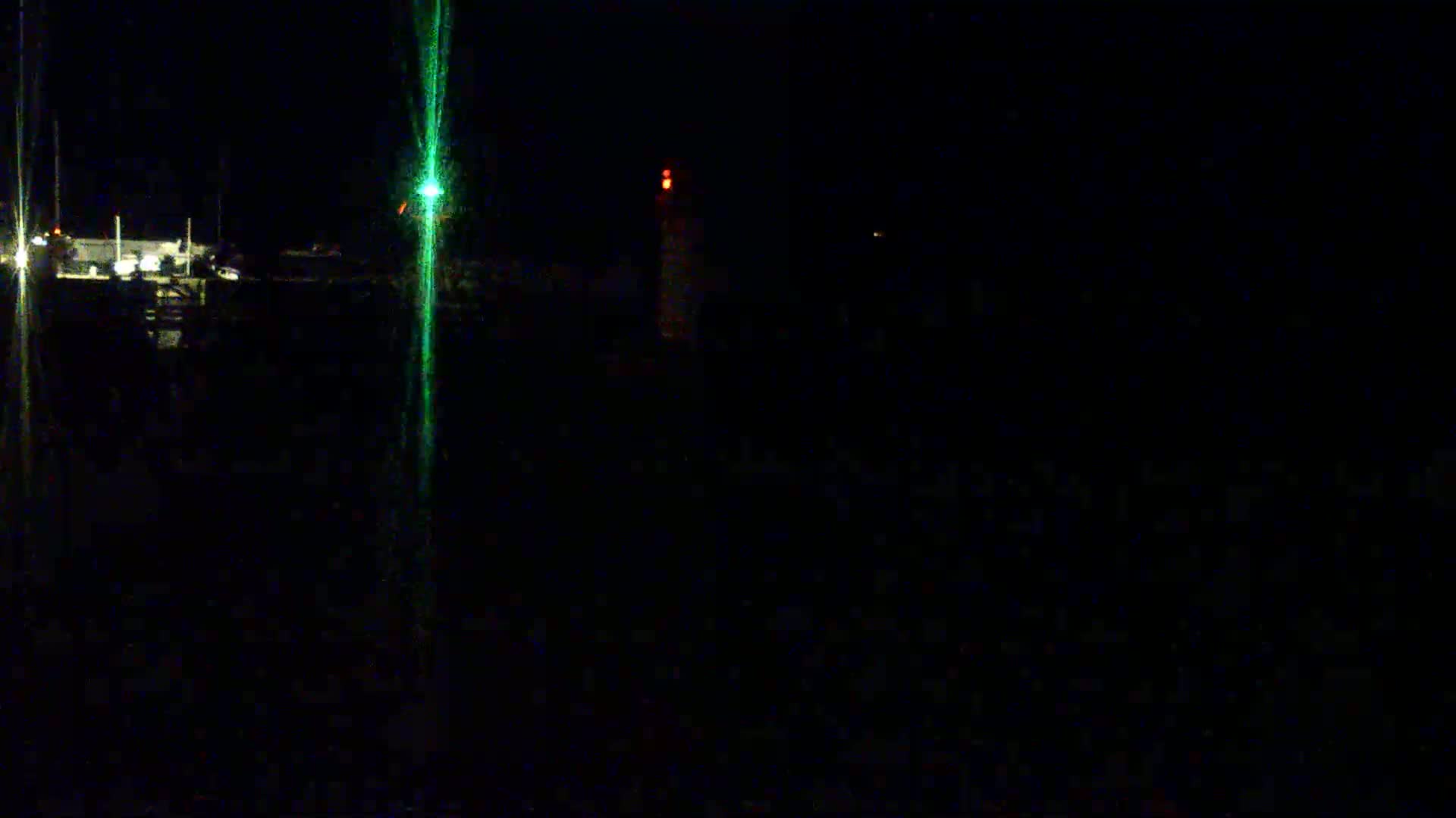 A nighttime view shows faintly lit boats and a dock with a green and a red light visible in the distance.