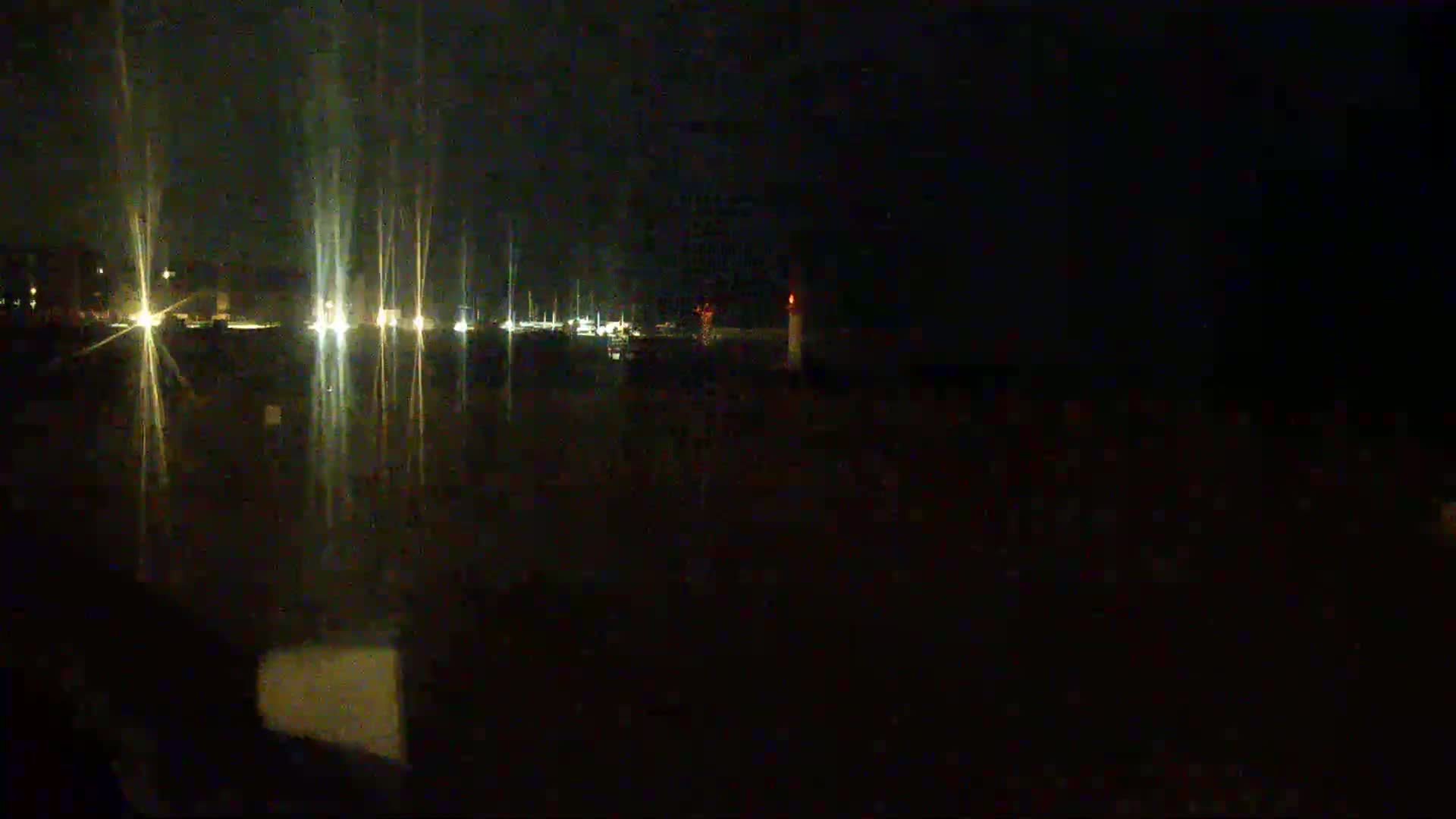 A nighttime view of a harbor with faintly visible boats and lights, and a lit structure in the distance.