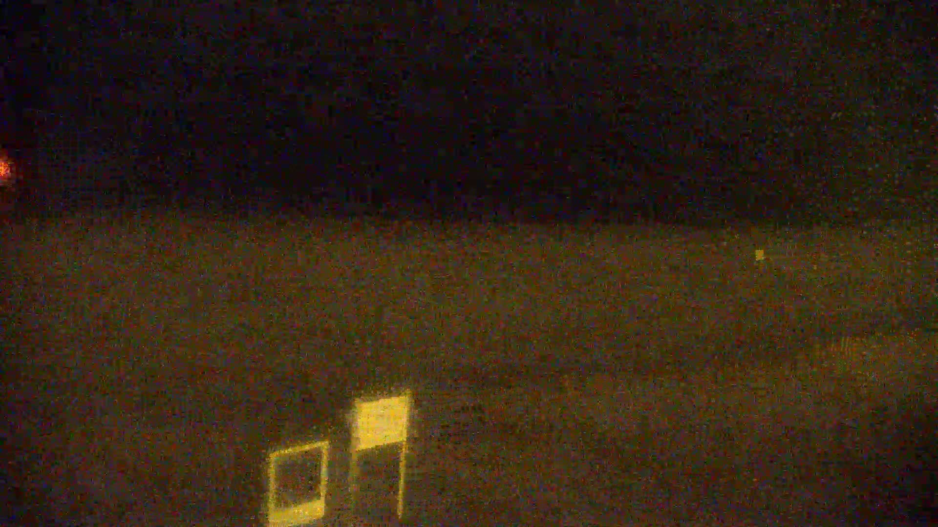A blurry, nighttime image shows a small, rectangular structure in the bottom right corner against a dark, possibly overcast sky with a faint orange light visible in the distance.