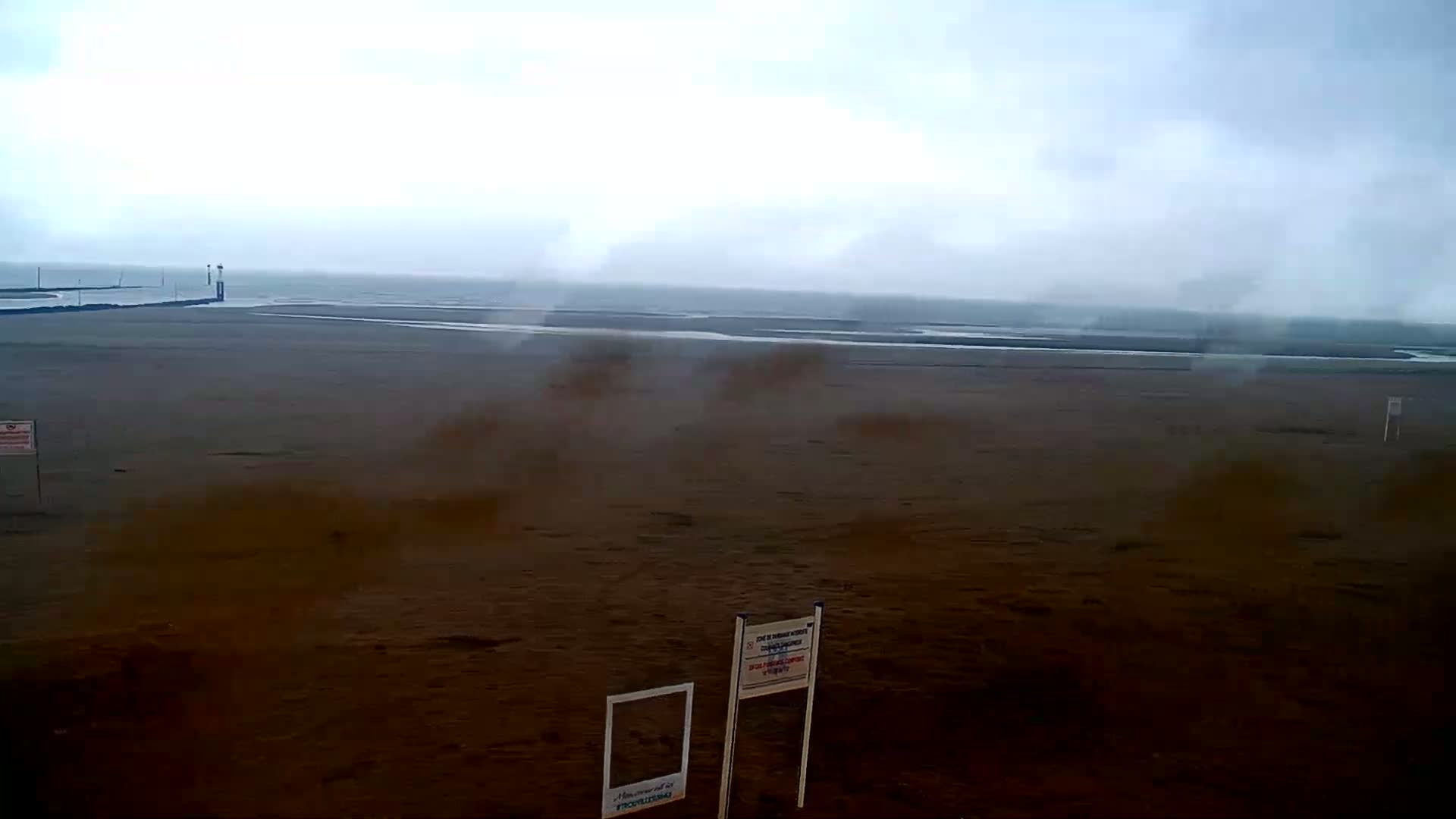 A wide shot of a sandy beach with a calm, overcast ocean in the background under a gray sky.