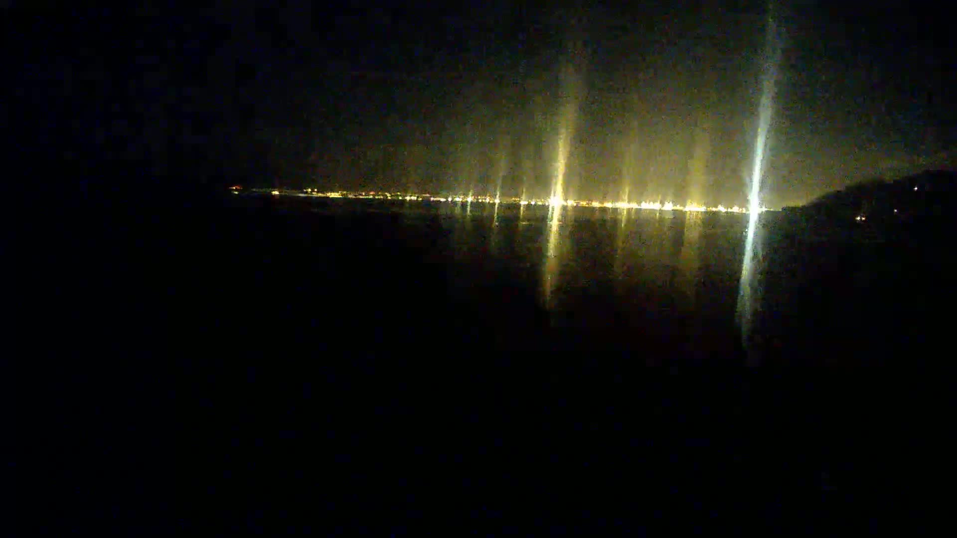 A distant city skyline is visible at night, its lights reflecting on a dark body of water.