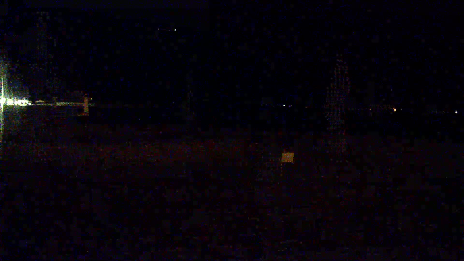 A dark, nighttime scene shows a flat, empty expanse of land with a few faint lights visible in the distance.