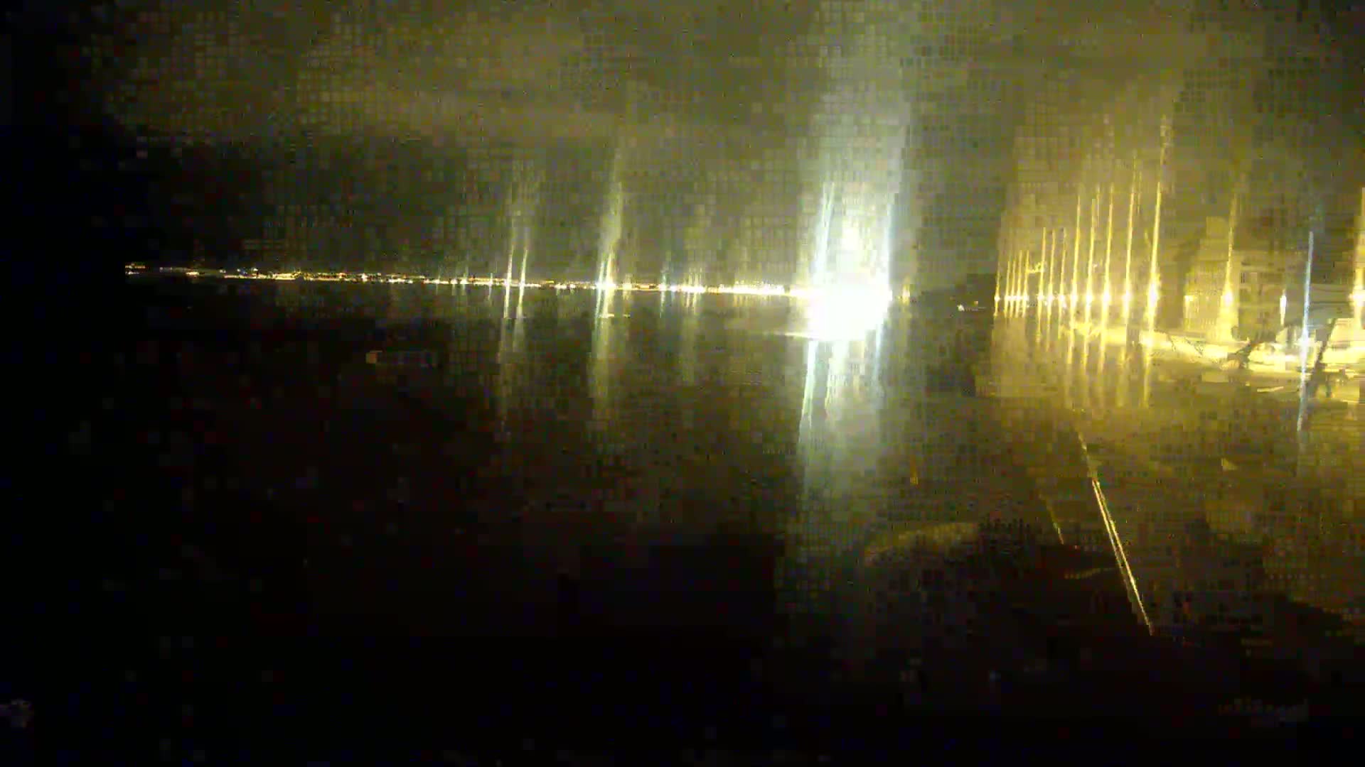 A nighttime view of a city's waterfront, reflecting lights on a dark, wet surface.