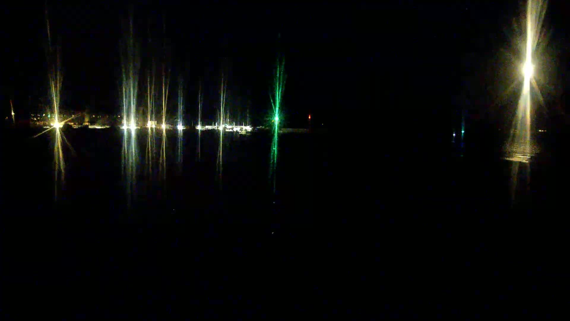 Reflected lights from a nighttime harbor illuminate a dark body of water.