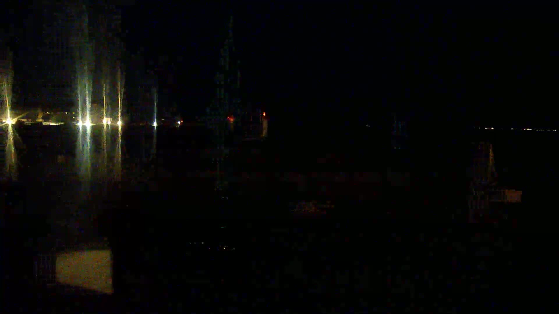 A dark nighttime scene shows several bright lights reflecting on a body of water.