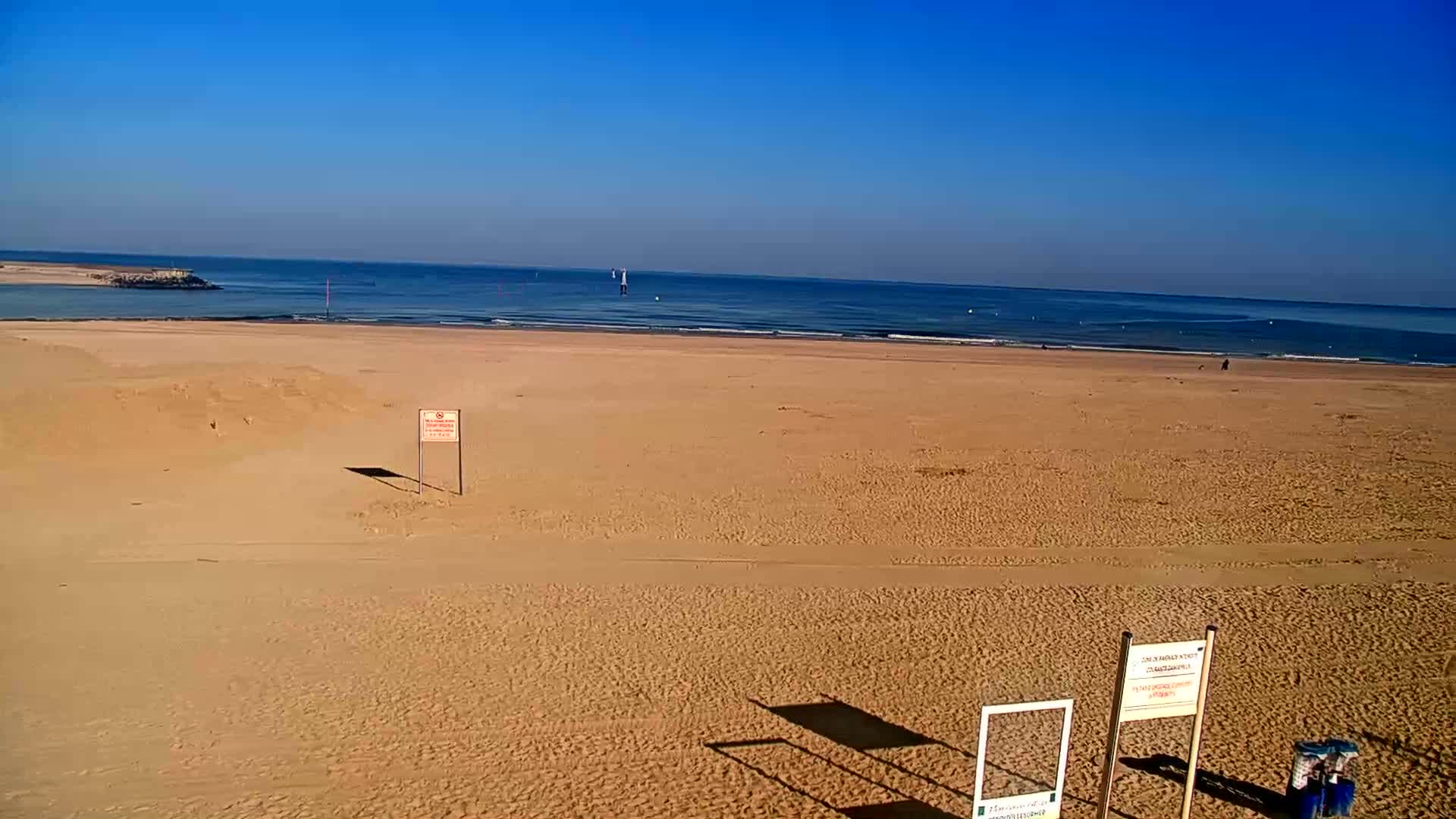 A wide sandy beach stretches to a calm ocean under a clear blue sky.