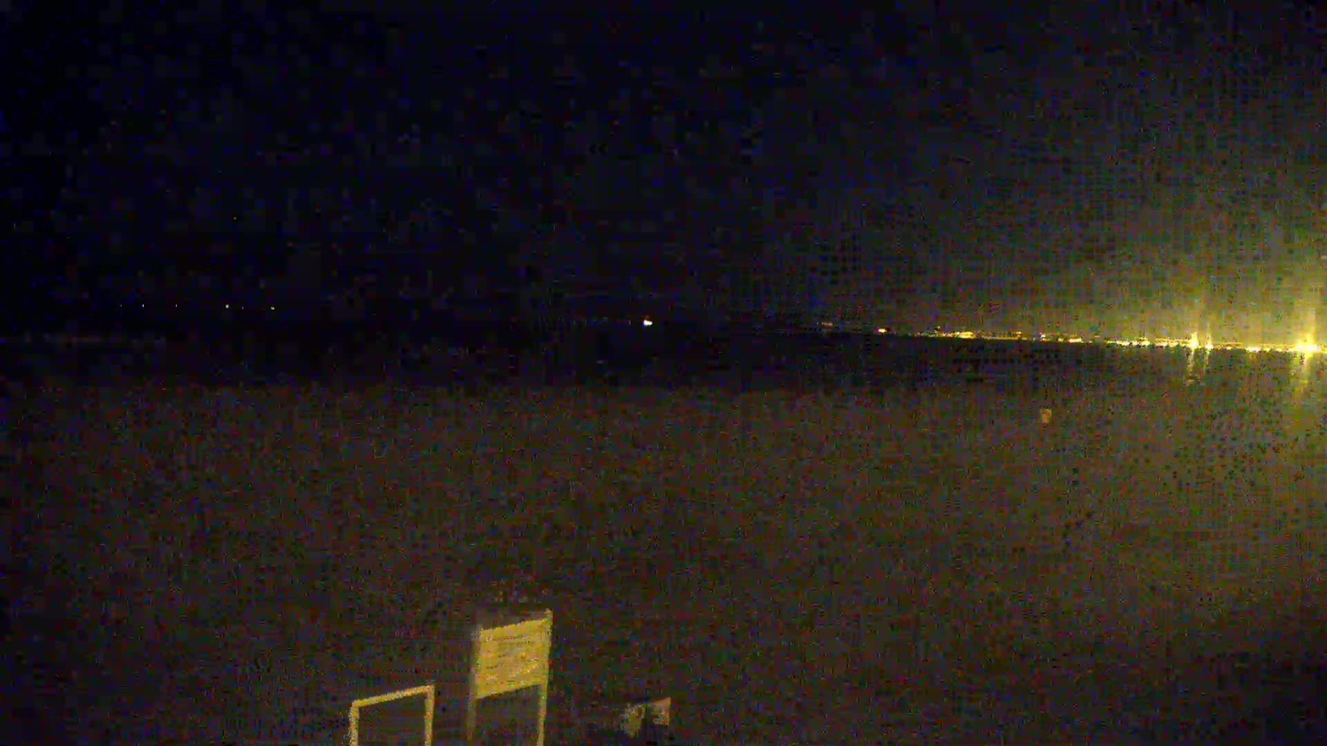 A dark, nighttime scene shows a flat expanse of land with distant city lights visible on the horizon.