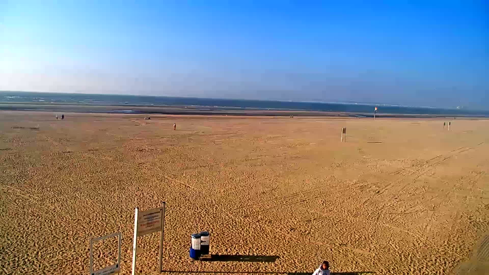 A wide, sandy beach stretches to a calm ocean under a clear blue sky.