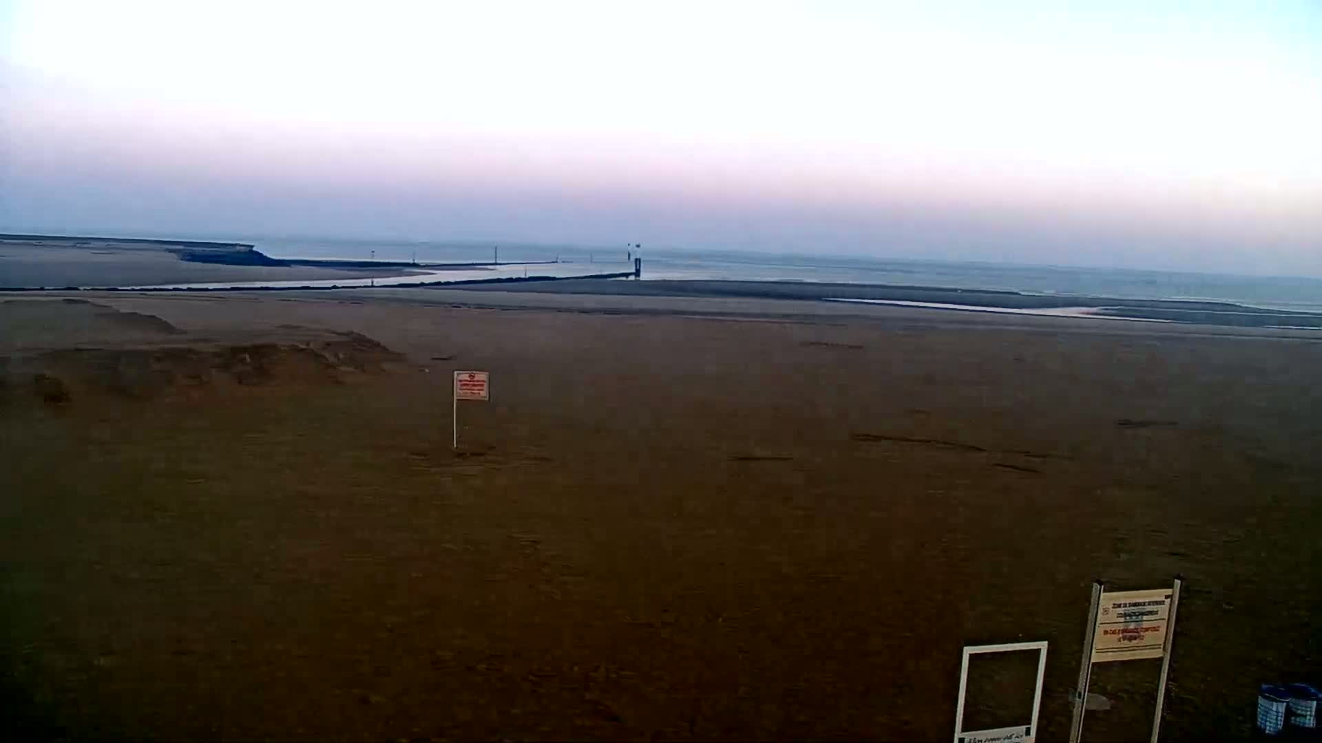 A wide, flat sandy beach stretches to a calm, gray-blue ocean under a pale, overcast sky.