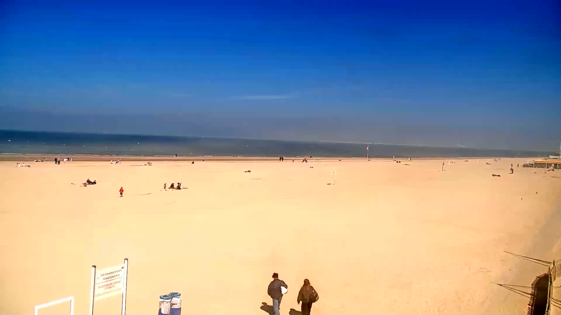 A wide sandy beach stretches to a calm ocean under a clear blue sky.