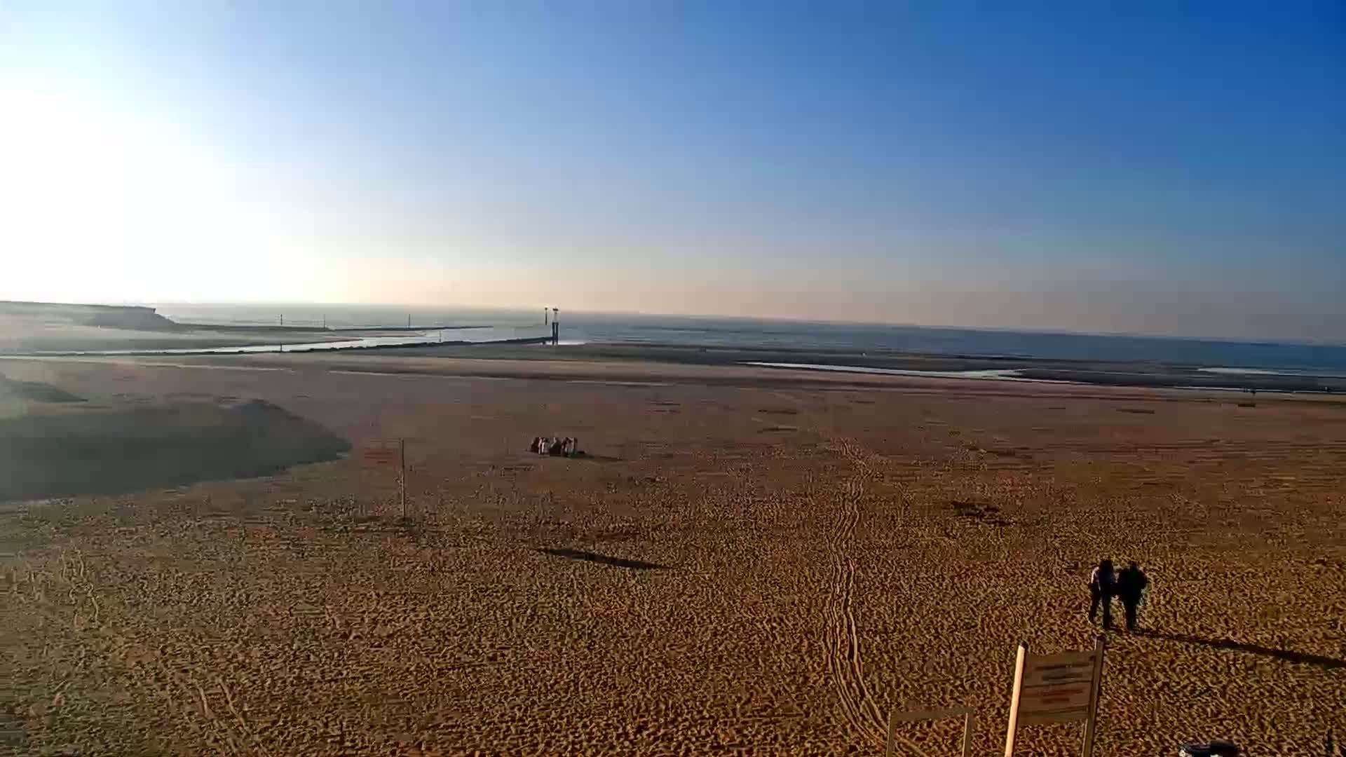 A wide expanse of sandy beach stretches to a calm ocean under a clear blue sky.