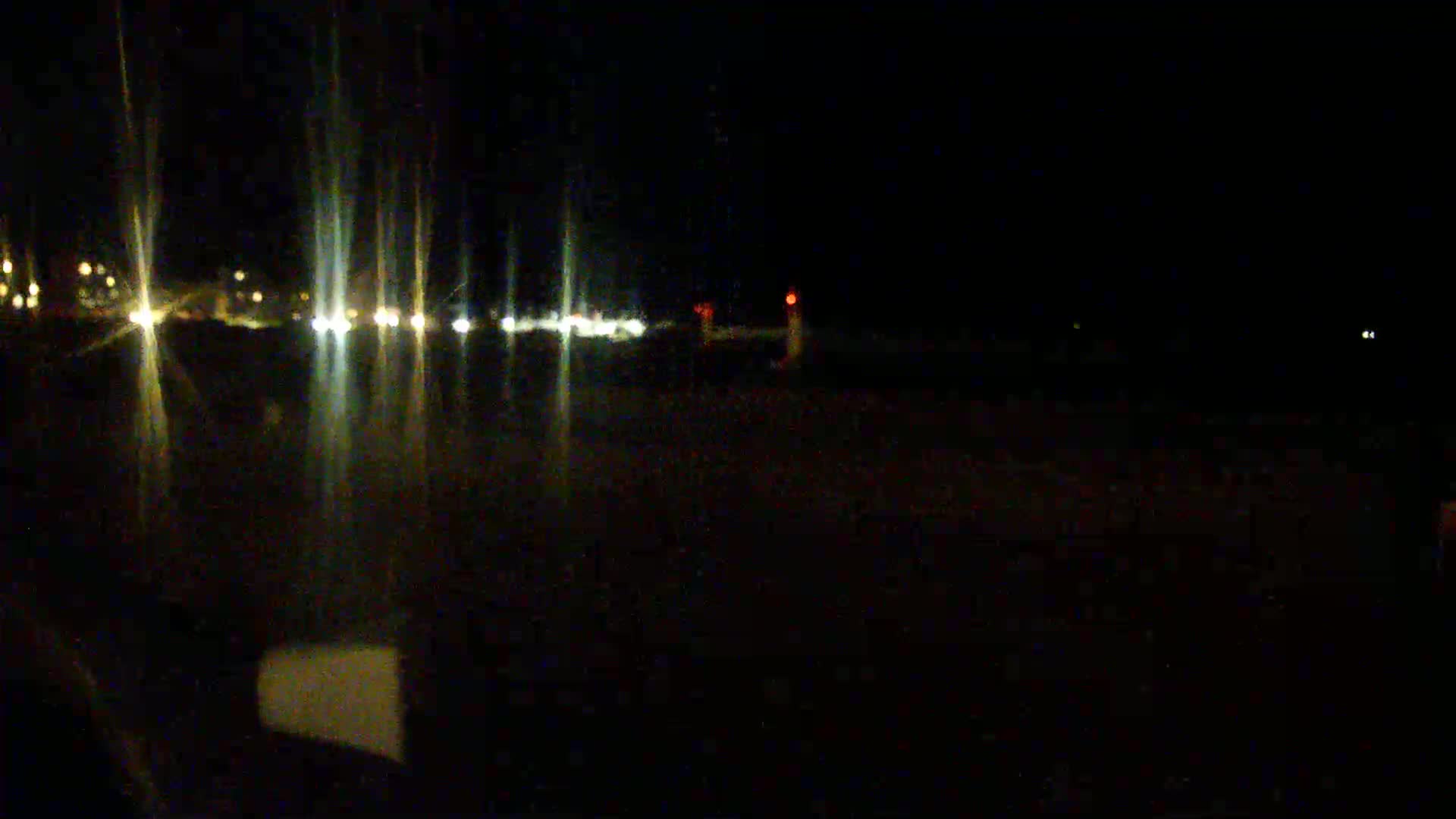 A nighttime view of a dark road with blurred headlights from oncoming traffic and faint lights in the distance.