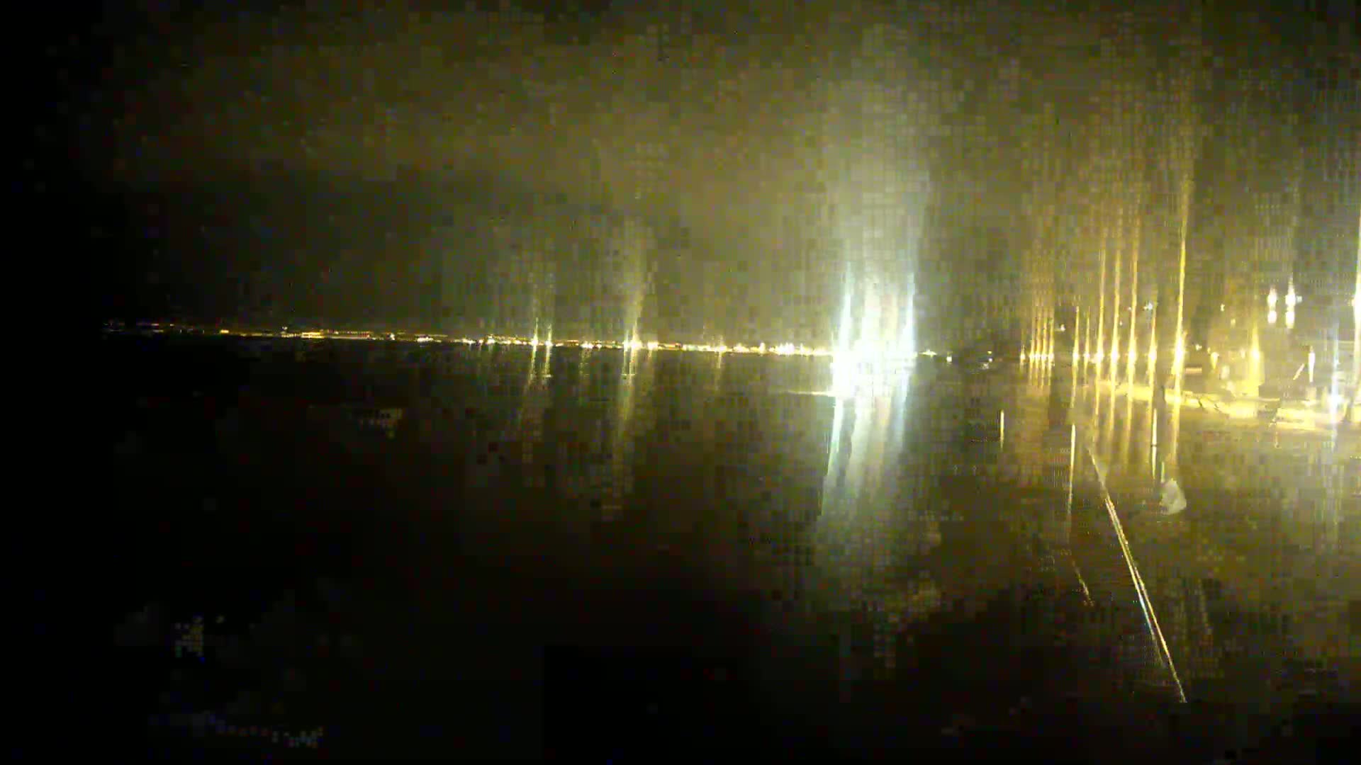 A nighttime view of a body of water reflecting the lights of a distant city under hazy or foggy conditions.