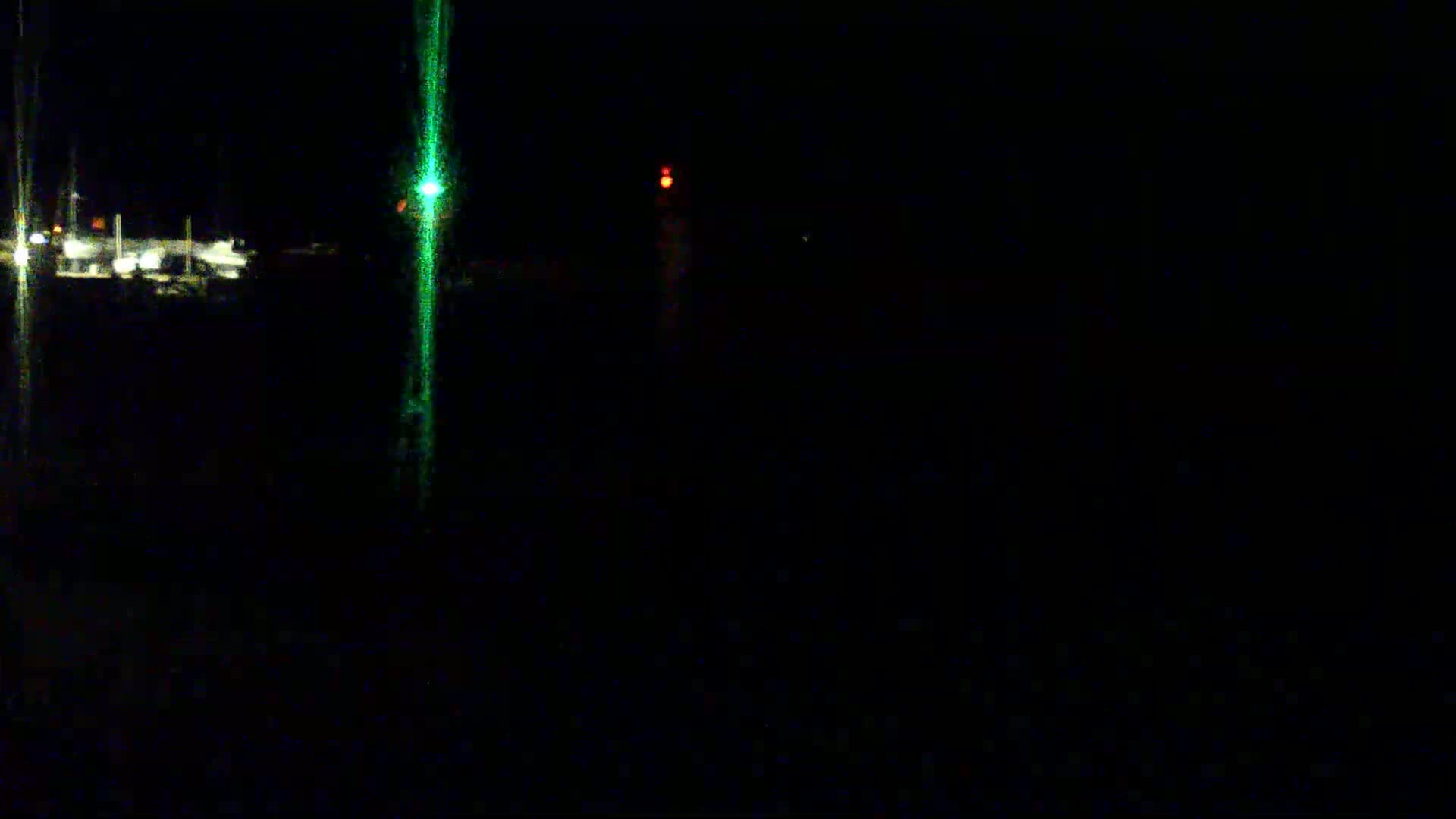 A nighttime, dark scene shows faint lights in the distance, with a vertical green light streak in the center.