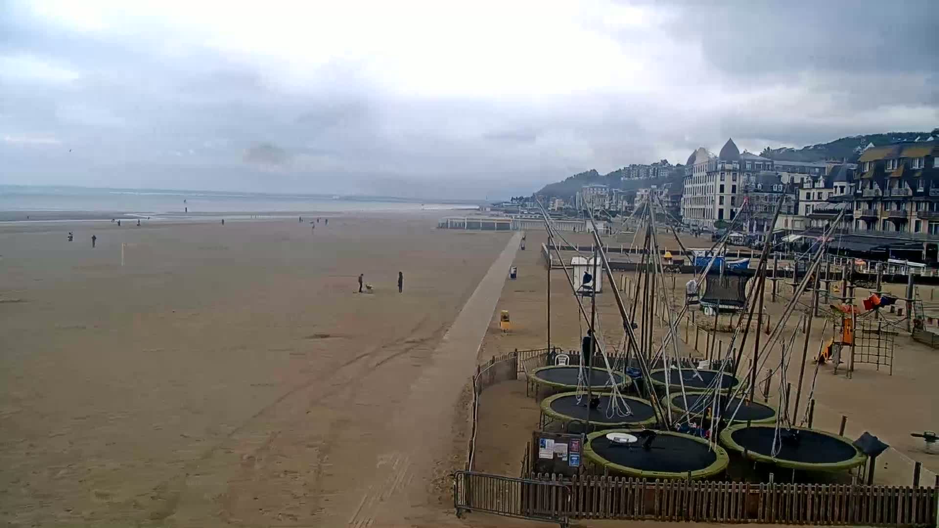 A sandy beach with several trampolines and a playground near buildings on a cloudy day.