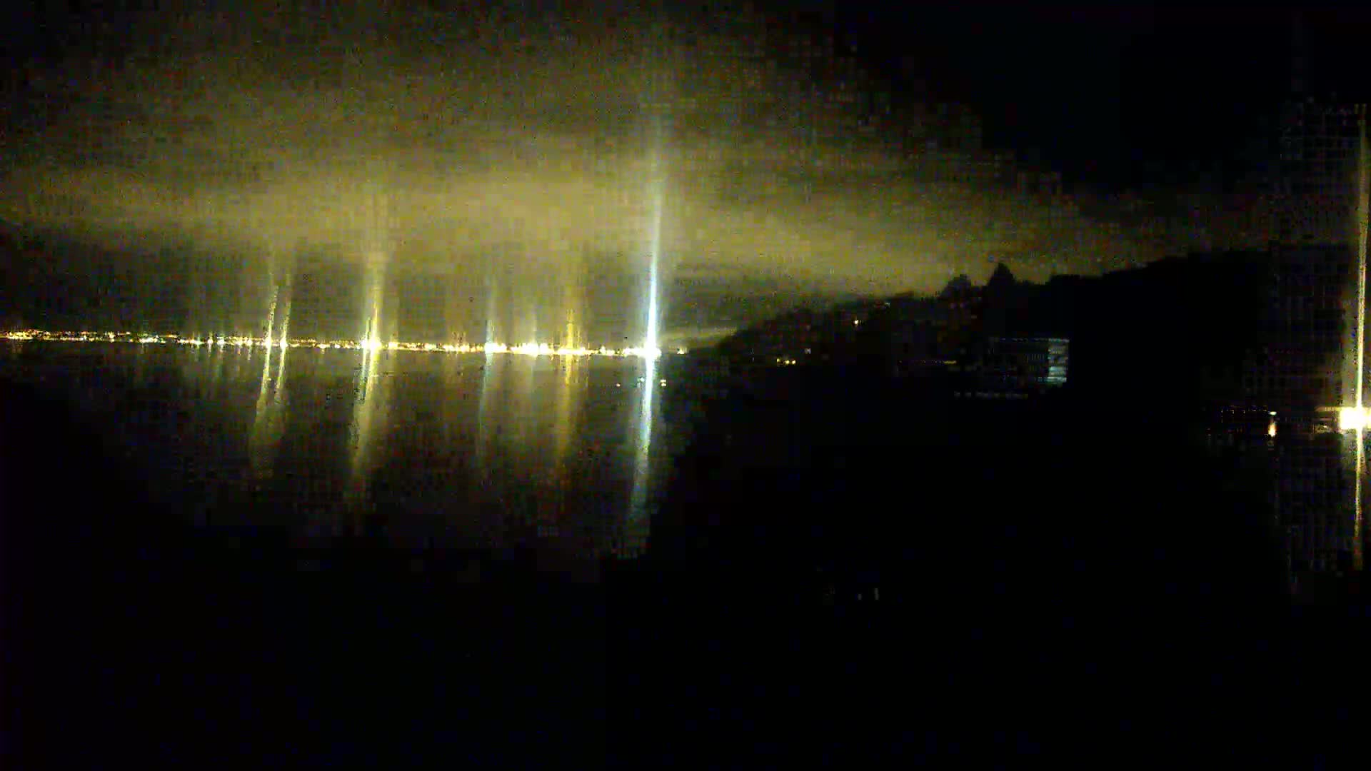 A nighttime view of a city's lights across a body of water under a cloudy sky.