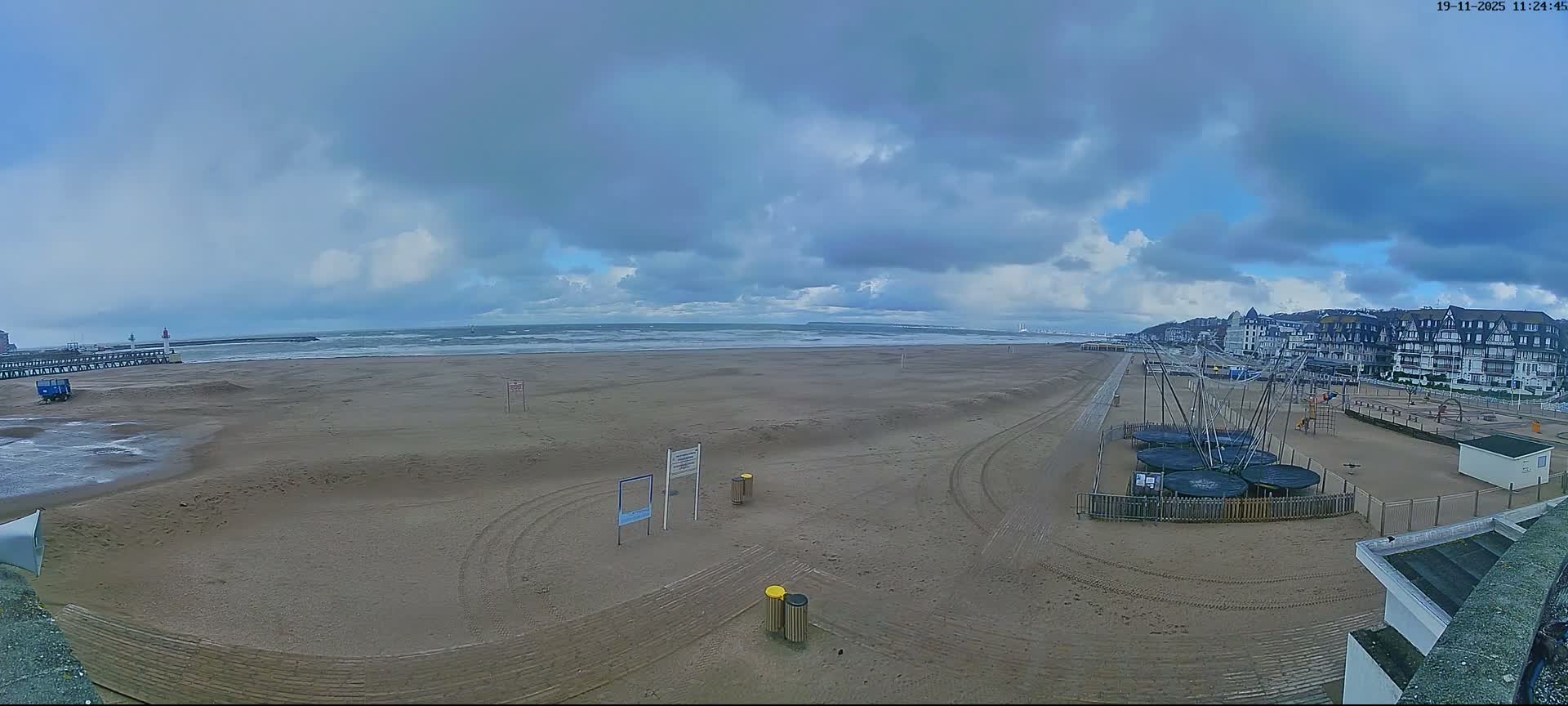 A nighttime view of a body of water reflecting the lights of a distant city and a closer shoreline with illuminated poles.