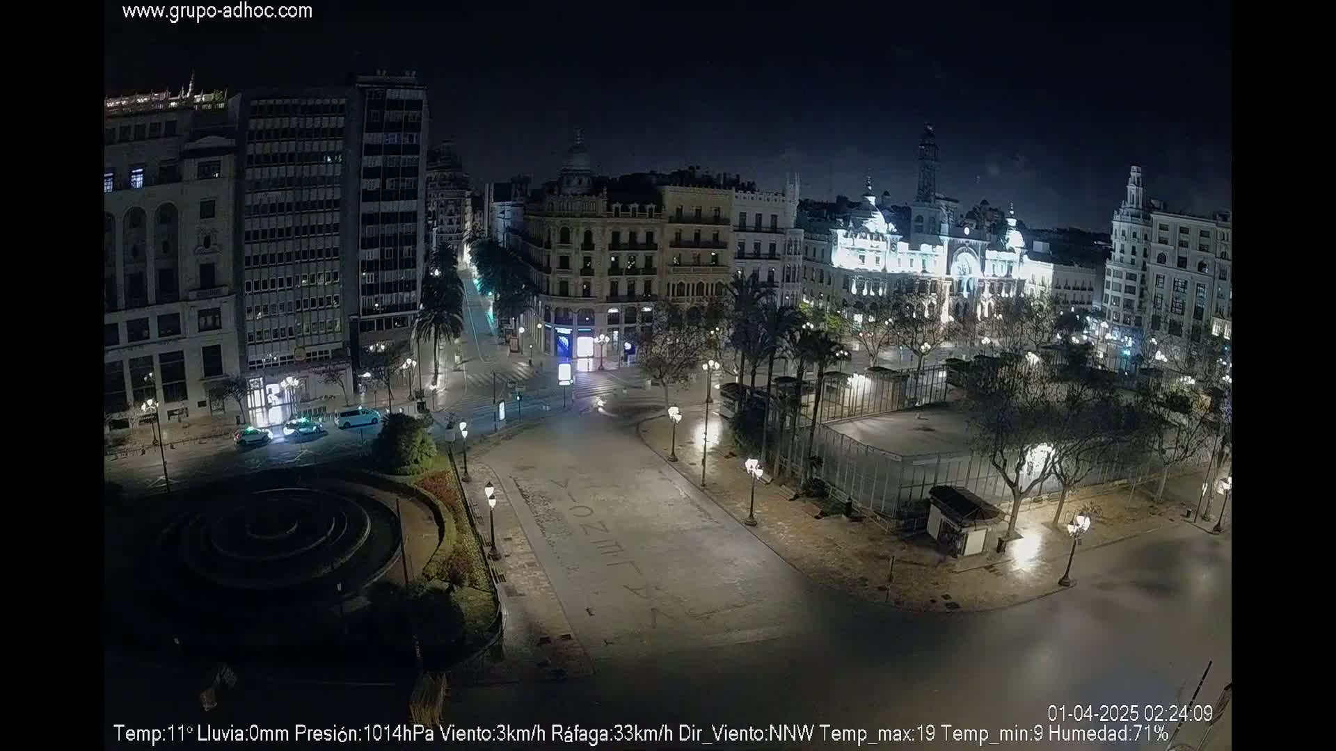 A nighttime, mostly empty city square with surrounding buildings is shown under a clear, dark sky.