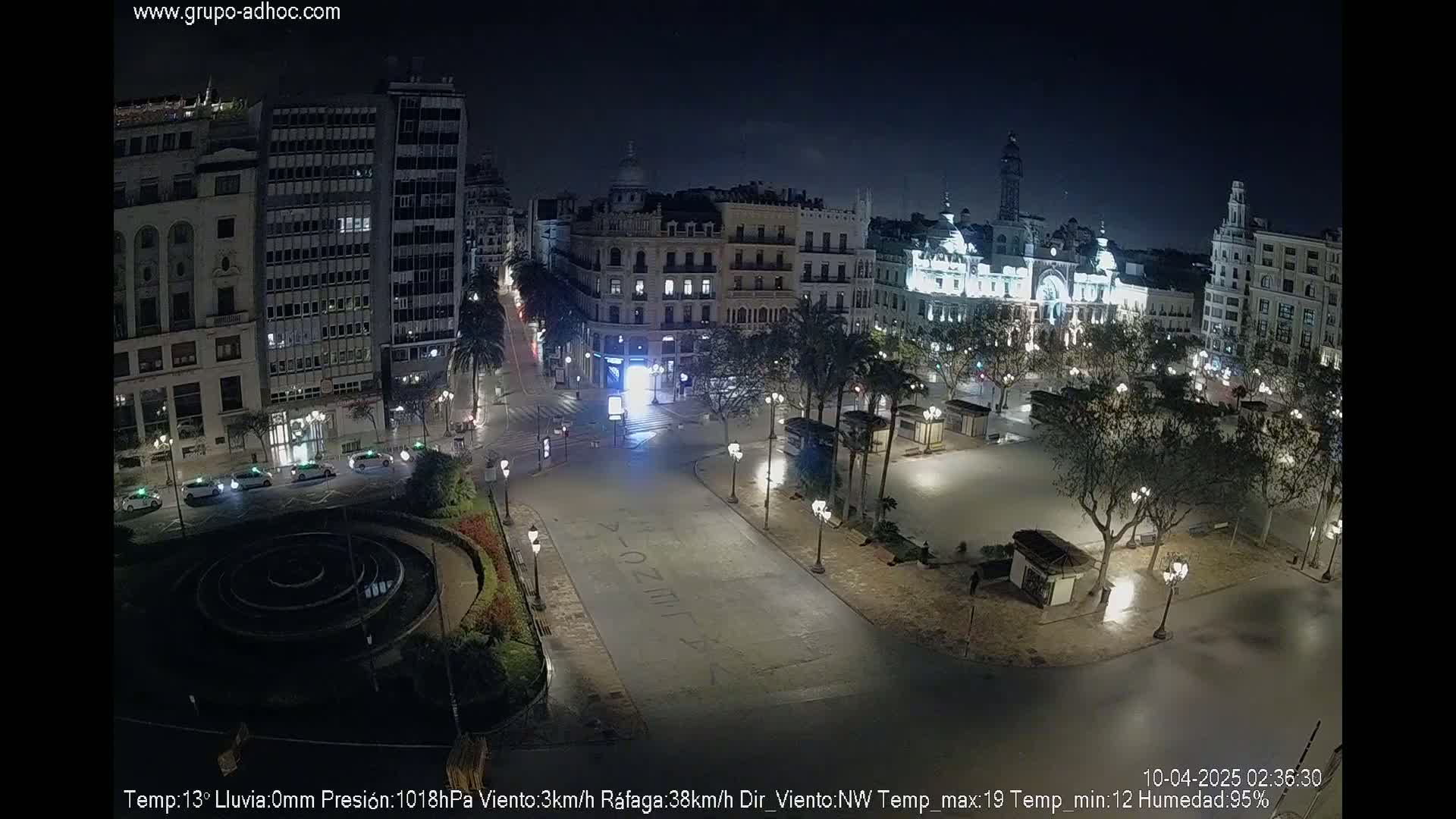 A nighttime view of a mostly empty city square surrounded by buildings, under a clear, dark sky.