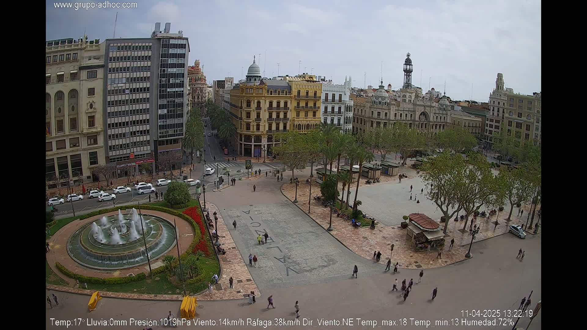 A city square with a fountain and surrounding buildings is shown on an overcast day.