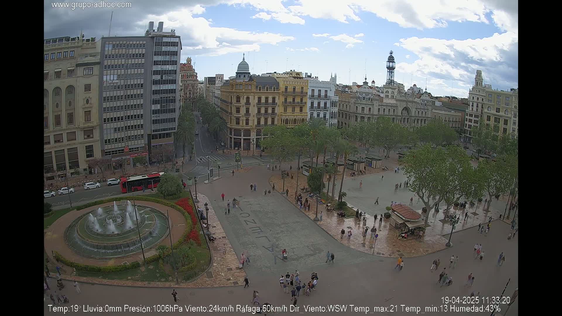 A city square with a fountain and surrounding buildings is viewed from above on an overcast day.