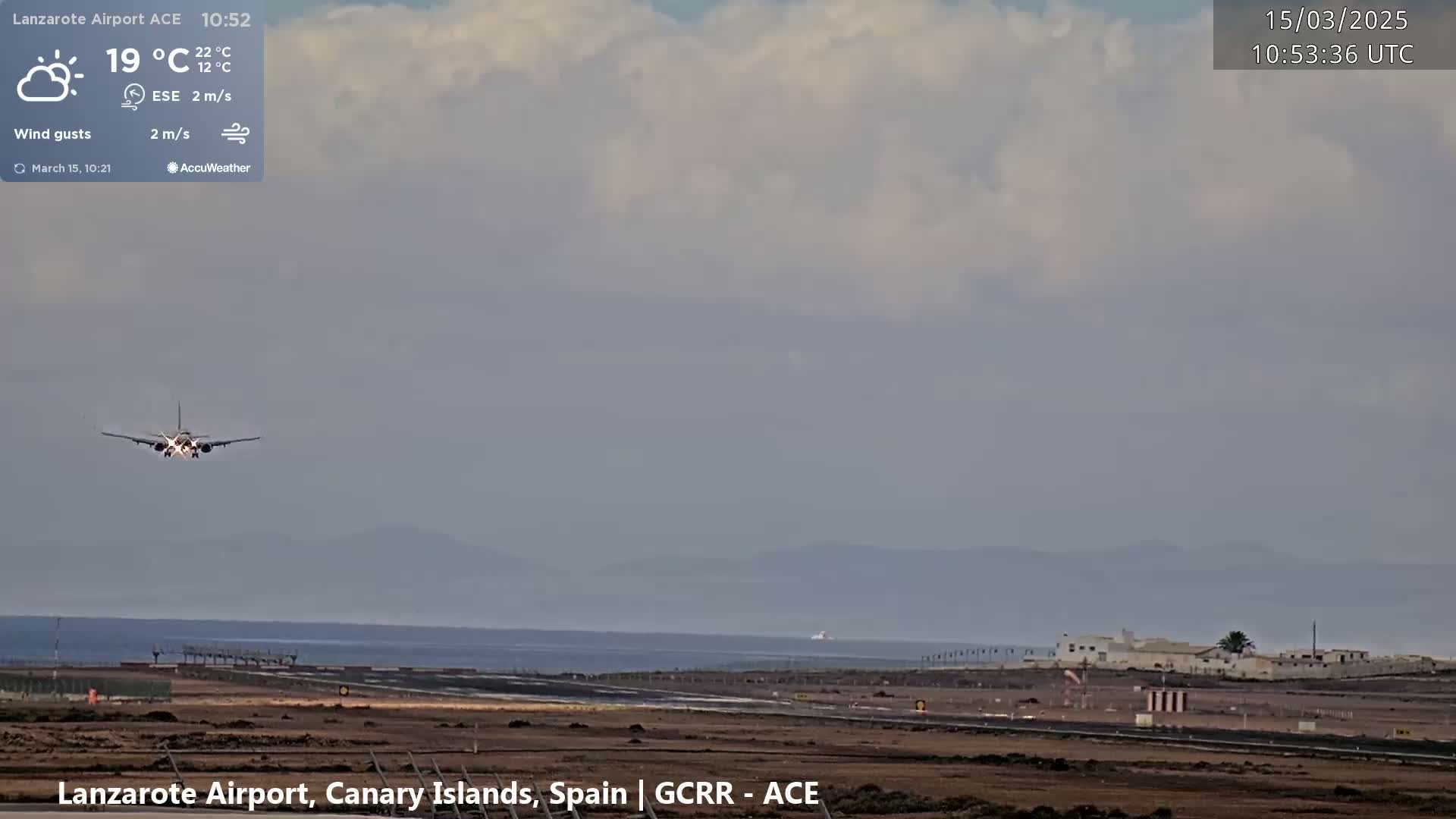 A passenger plane is landing at an airport near a body of water under partly cloudy skies.