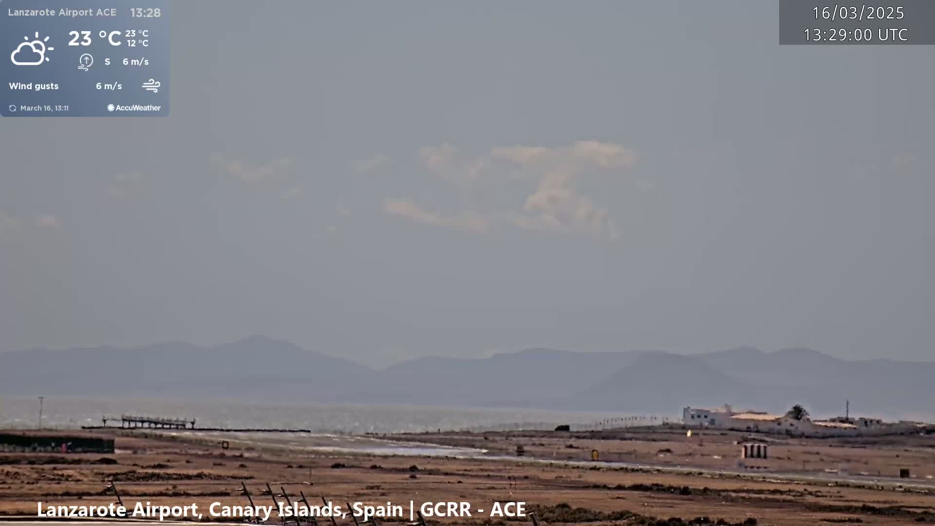 A mostly clear, hazy day with light winds shows a view of an airport with a body of water and distant mountains in the background.