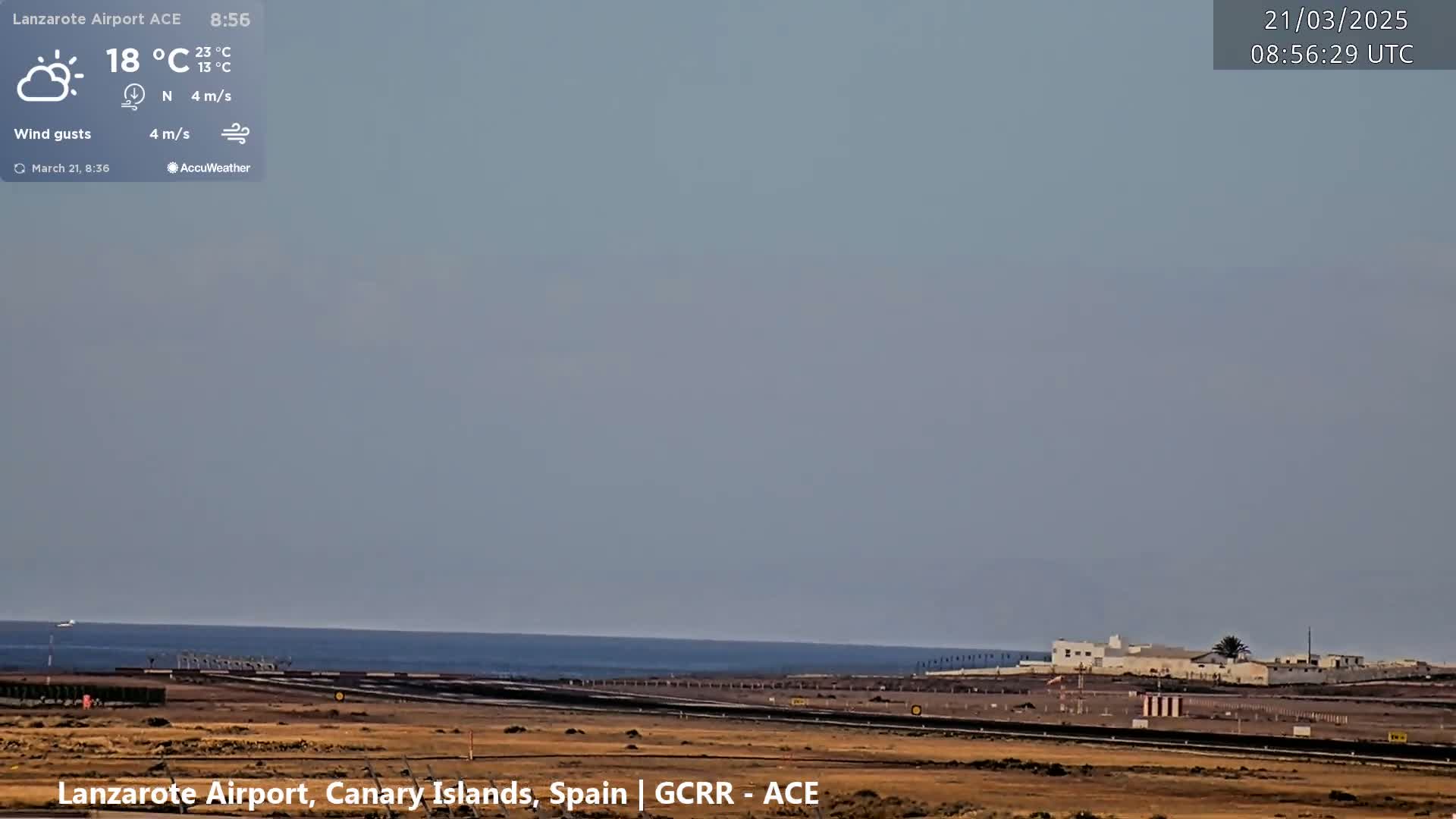 A partly sunny, hazy day with a light northerly wind shows an airport runway near the ocean.