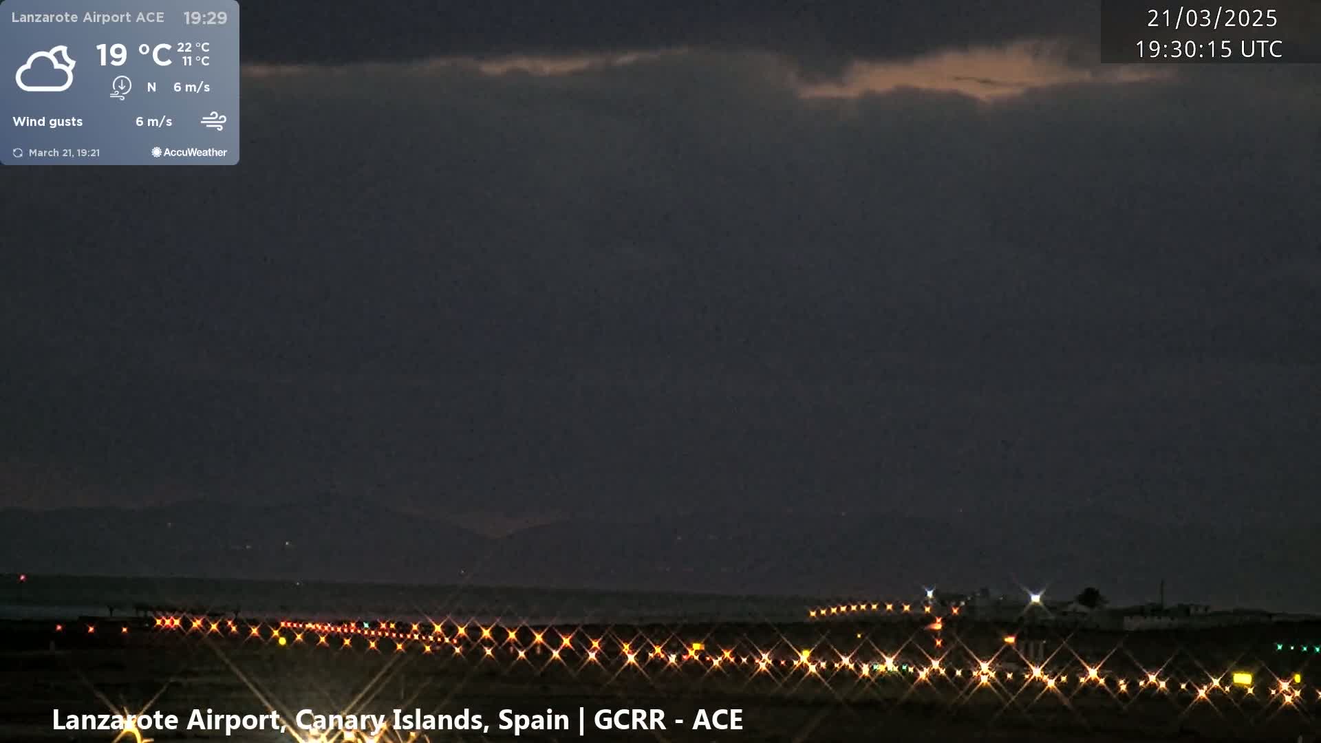 A nighttime view of an airport runway illuminated with lights under a dark, cloudy sky.