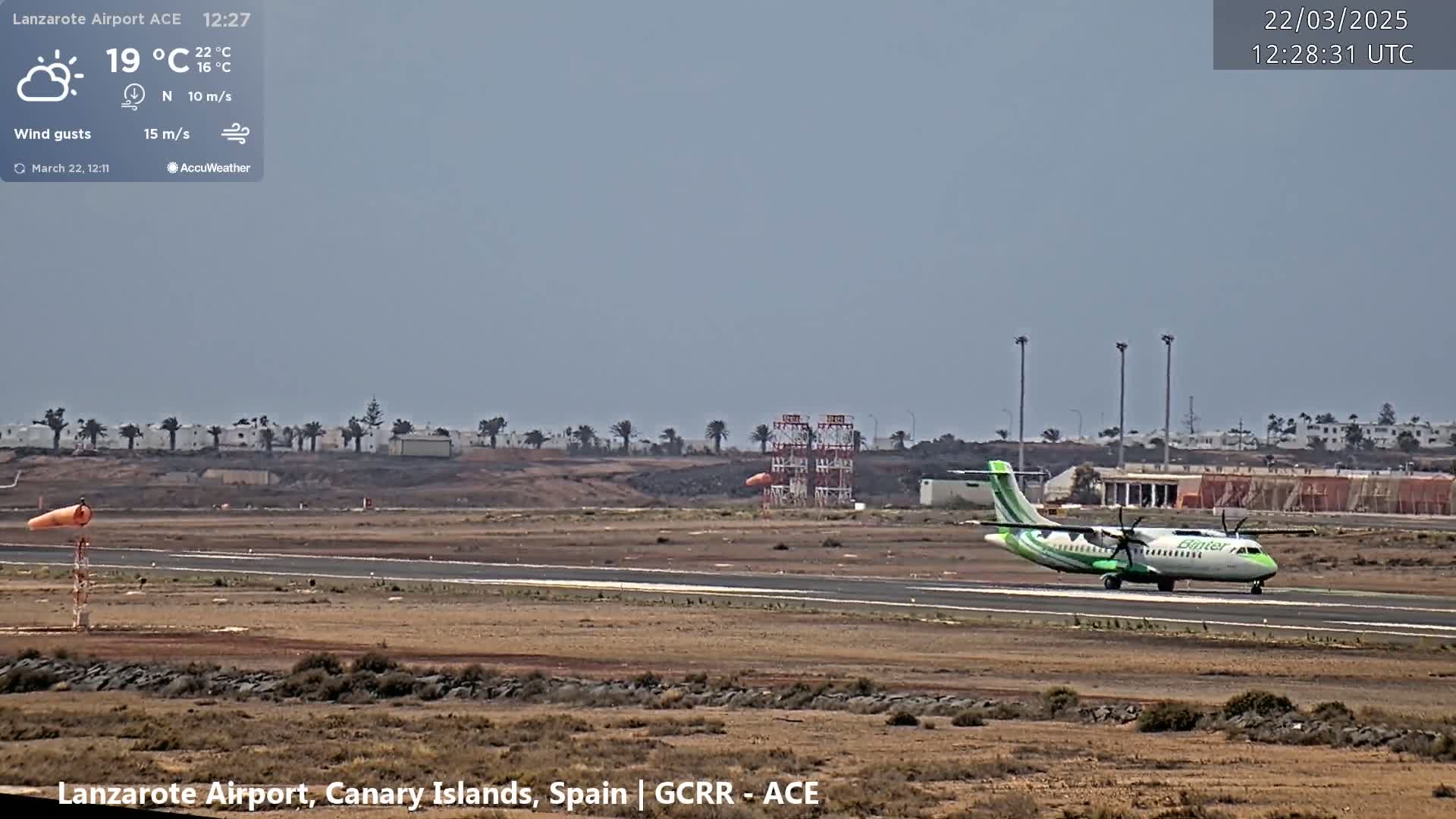 A propeller plane taxis on a runway at an airport under partly sunny skies with a light wind.