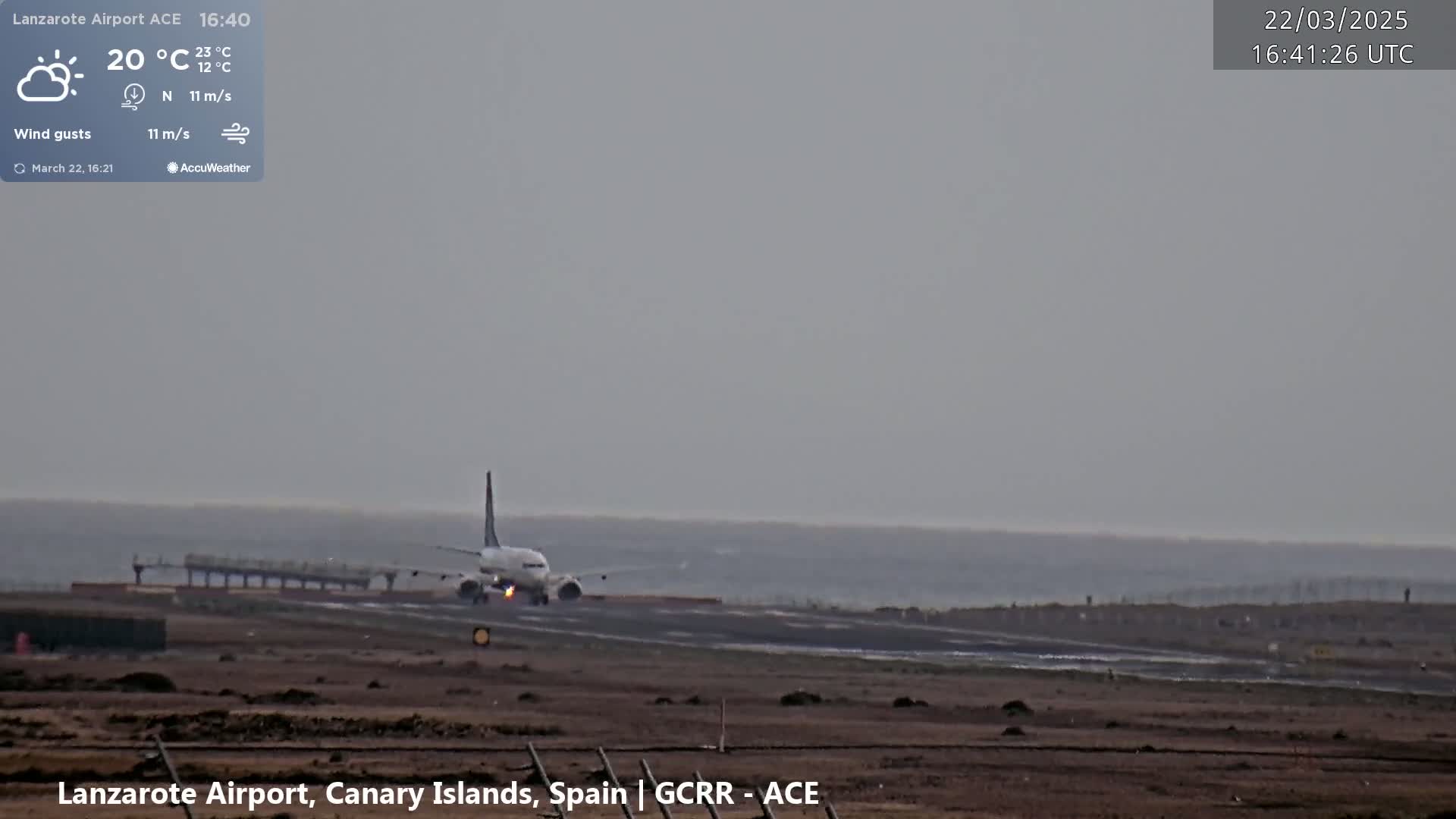 A passenger airplane is landing on a runway near a body of water under hazy, overcast conditions.