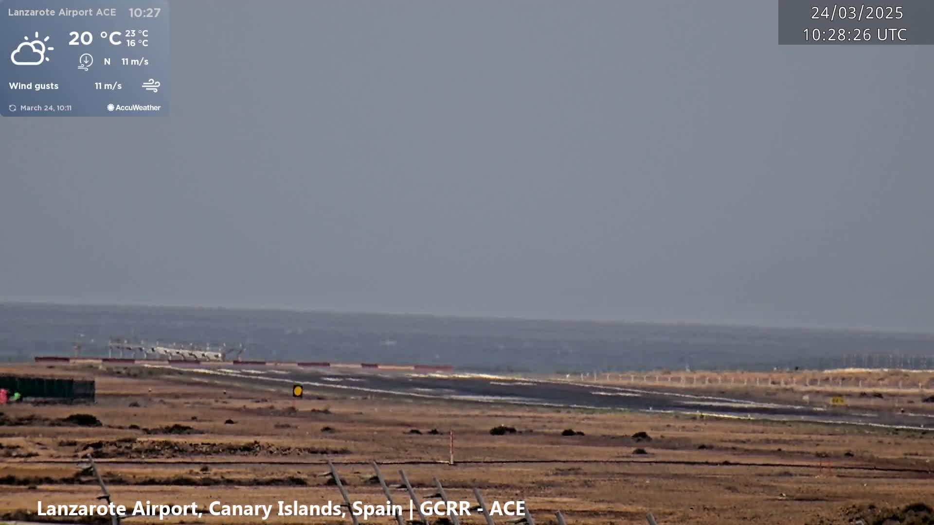 A mostly clear, windy day is shown at an airport with a runway, and an expanse of ocean visible in the distance.