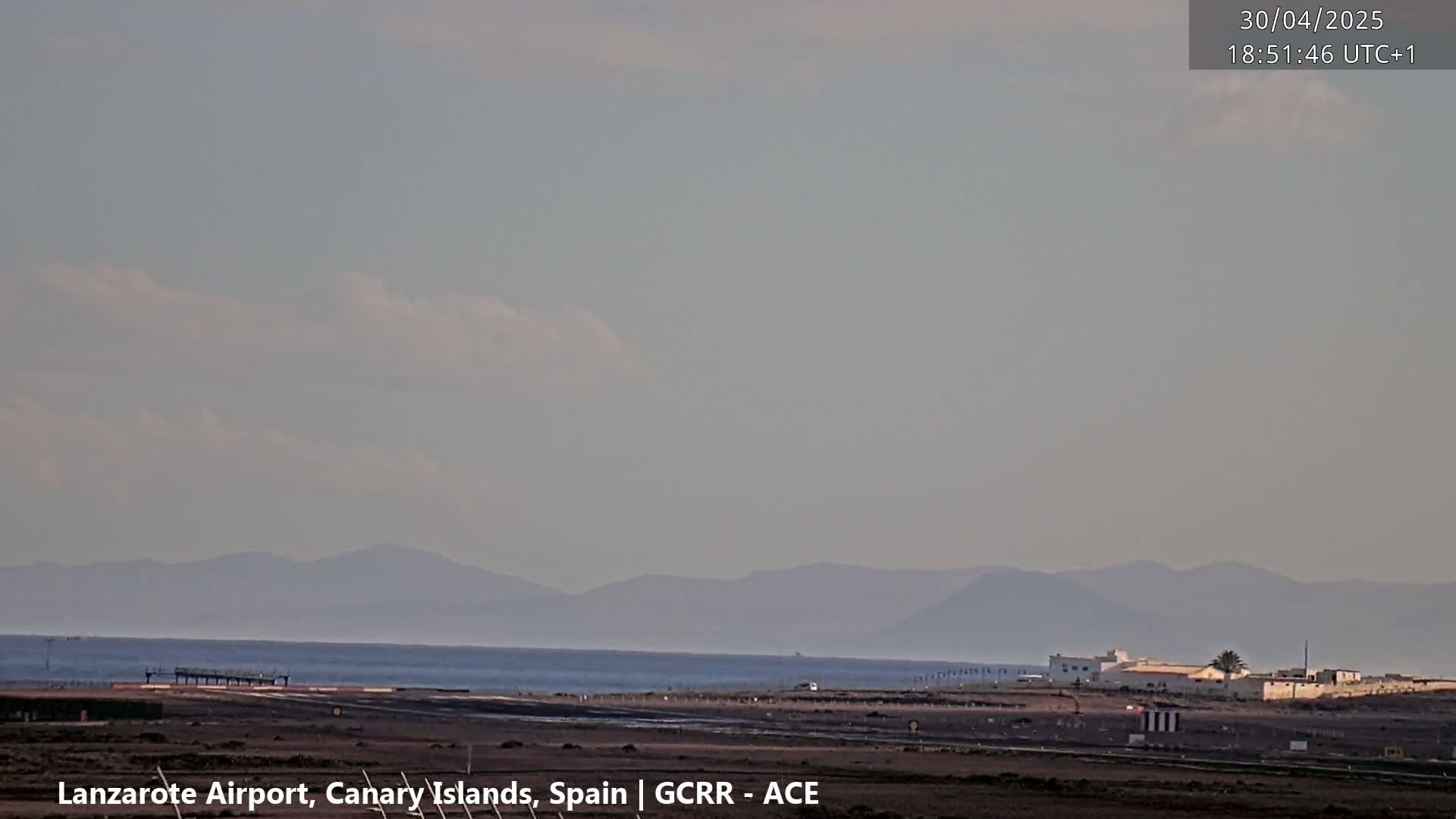 A hazy, overcast sky overlooks a calm ocean with distant mountains, and a runway at an airport.